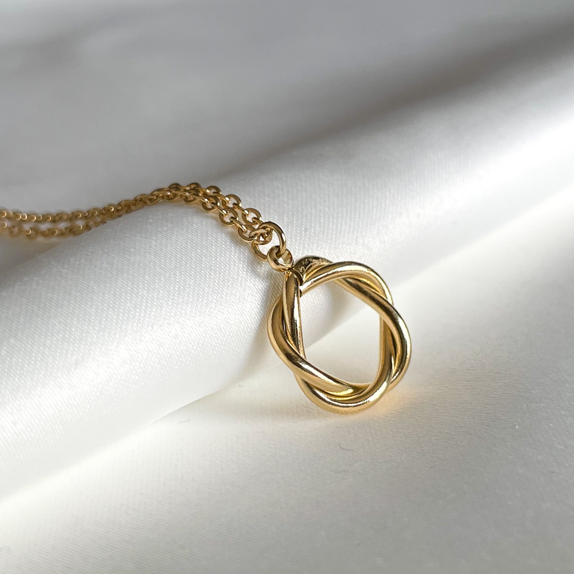 Gold necklace with a knot circle pendant on a white fabric background
