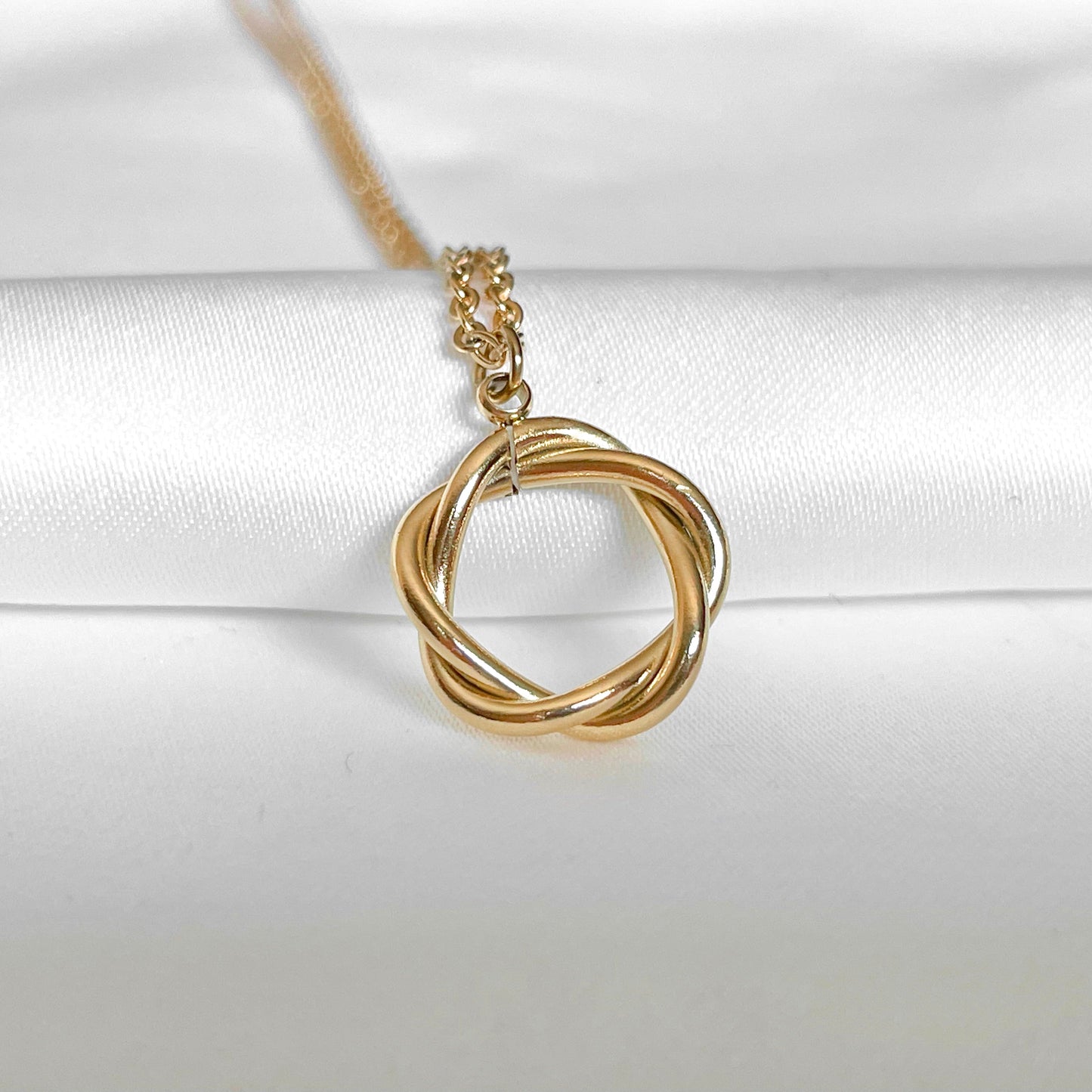 Gold necklace with a entwined circle pendant on a white satin background
