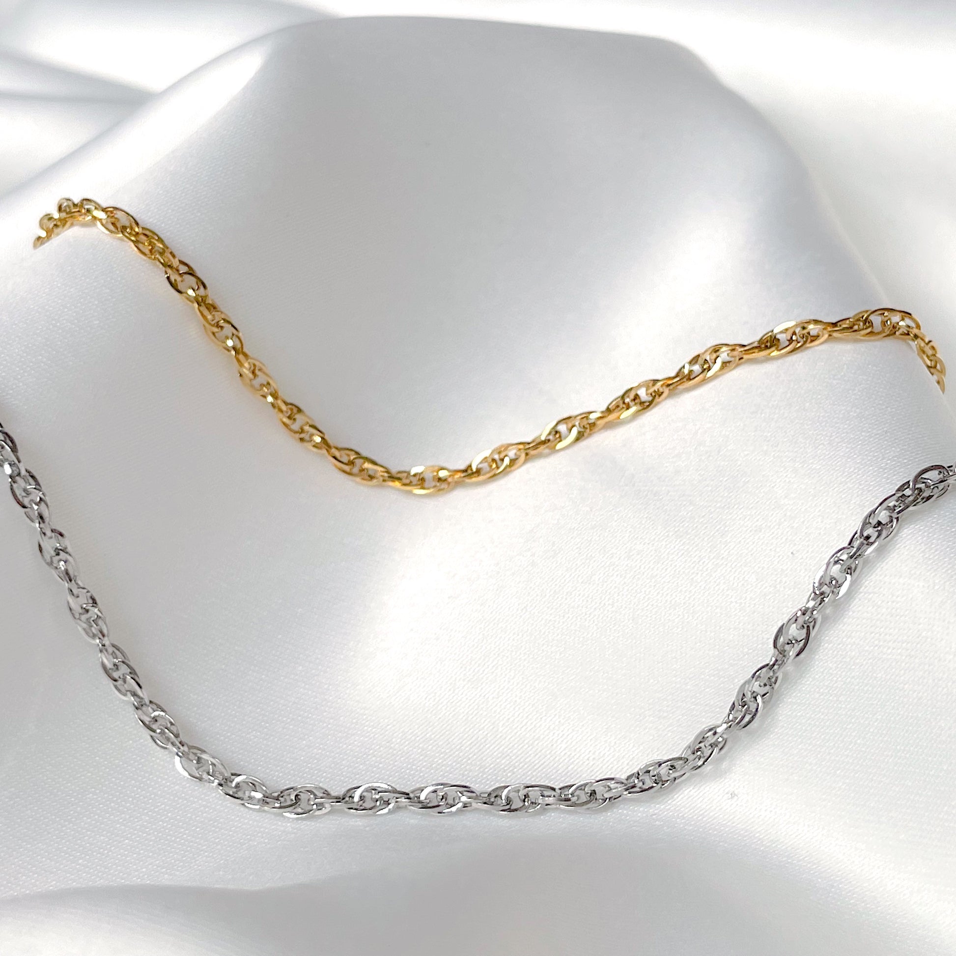 Gold and silver twisted chain anklets on a white fabric background