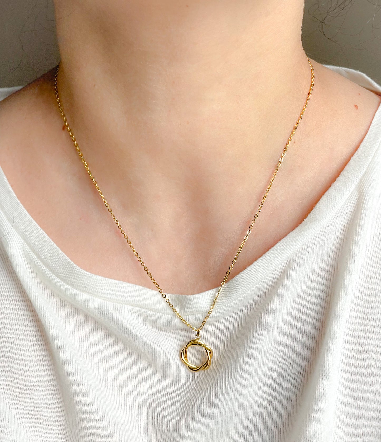Gold necklace with a small twisted circle pendant on a white shirt
