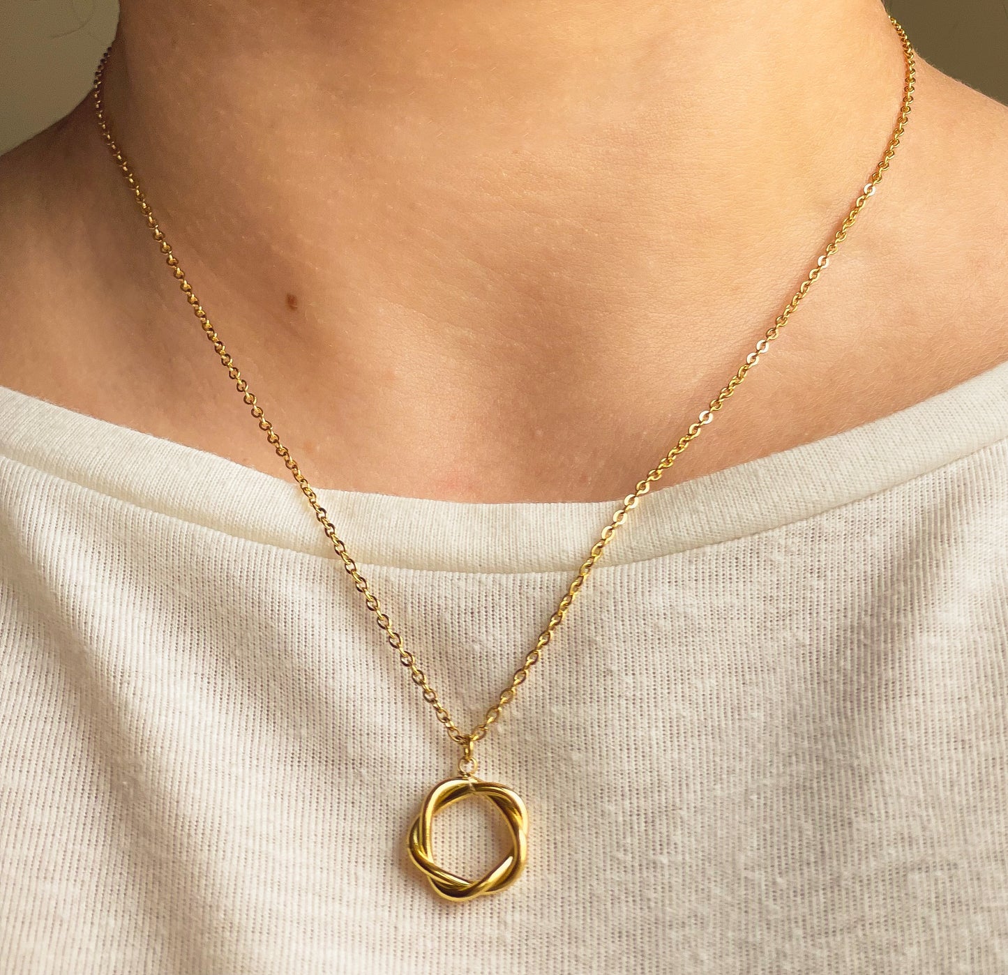 Gold necklace with a entwined circle pendant on a person wearing a white top.