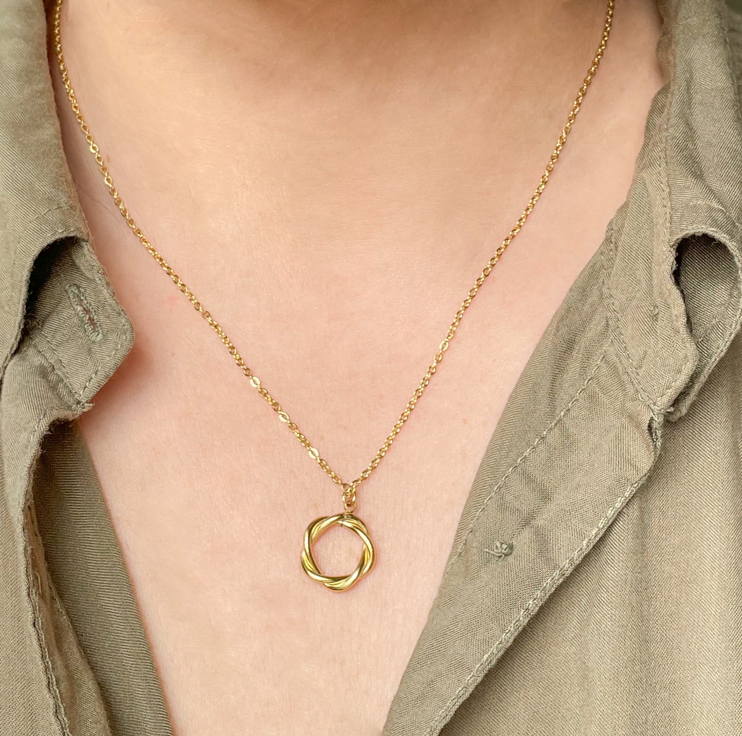 Gold necklace with a circular pendant worn by a person in a green shirt.