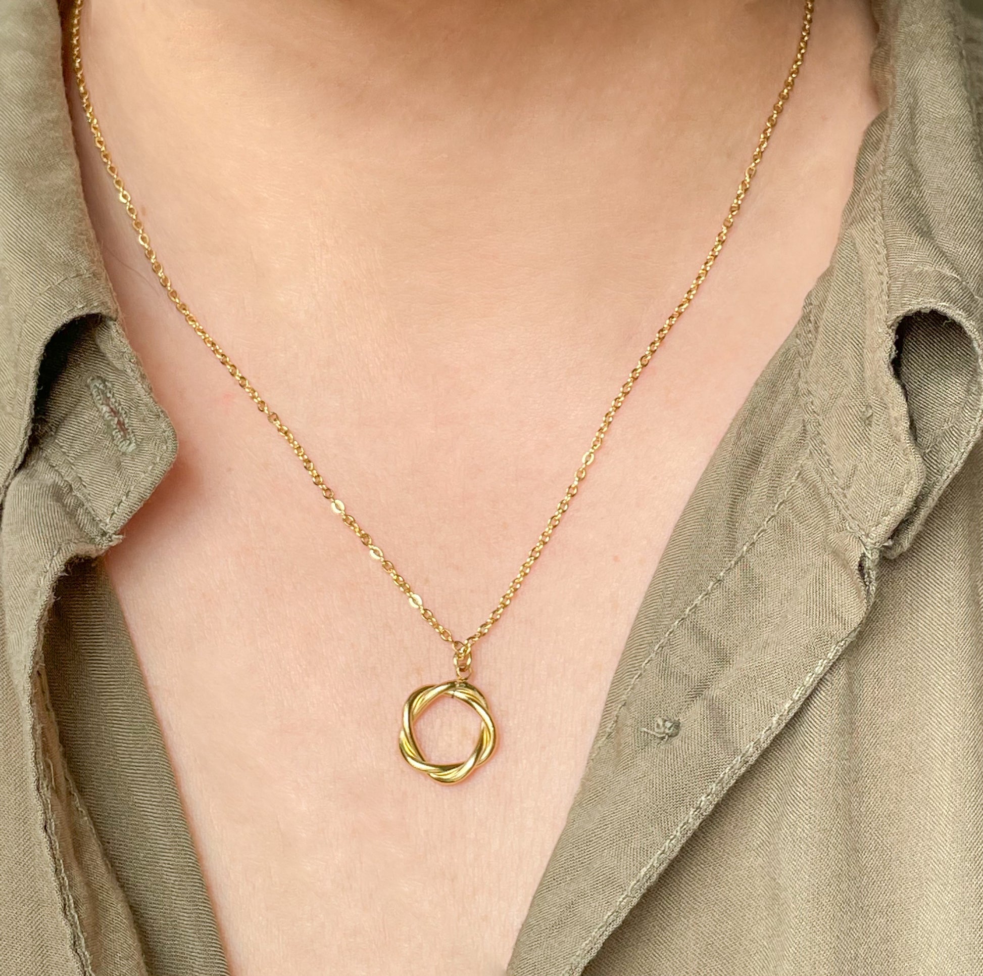 Gold necklace with a circular pendant worn by a person in a green shirt.