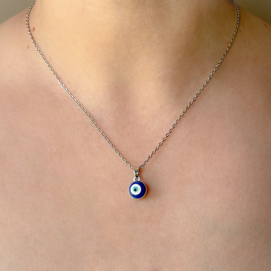 Silver necklace with a round blue evil eye pendant worn by a person
