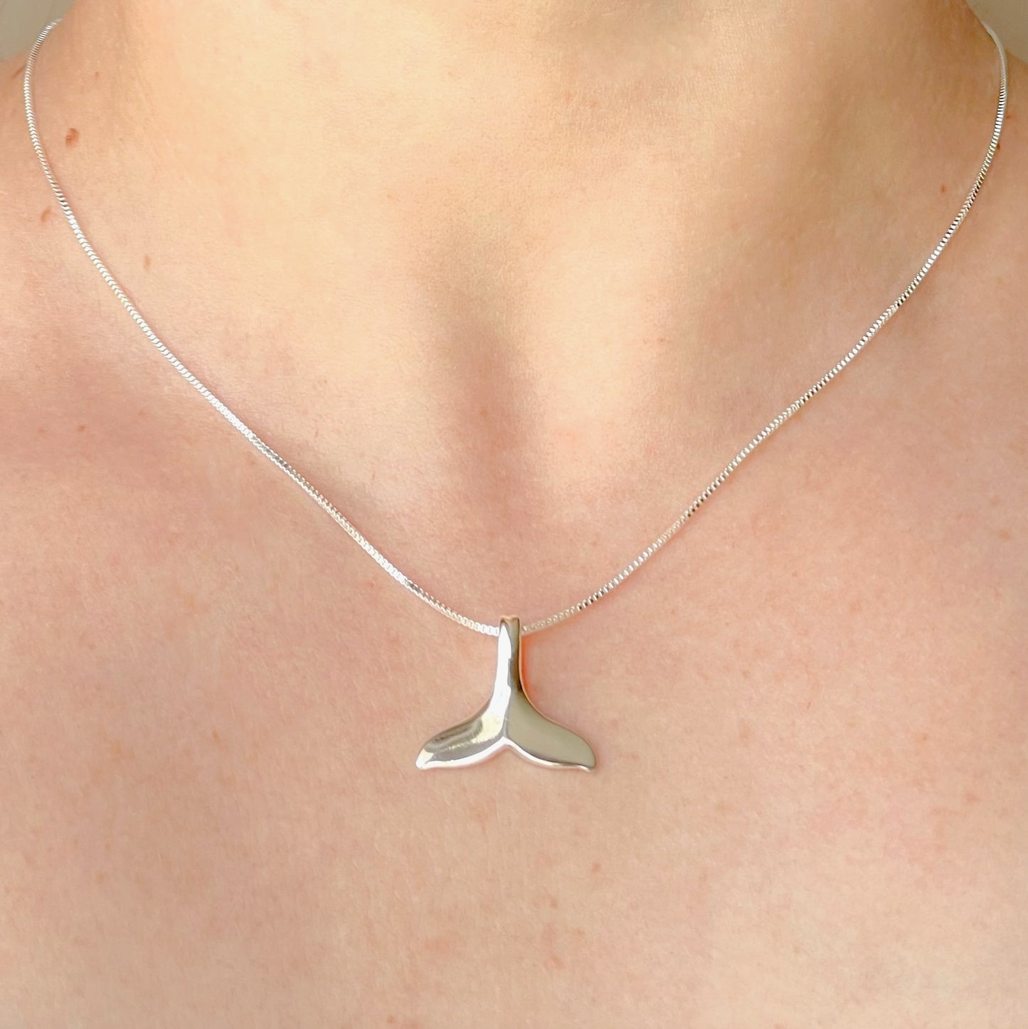 Silver whale tail necklace on a thin box chain on a person's neck