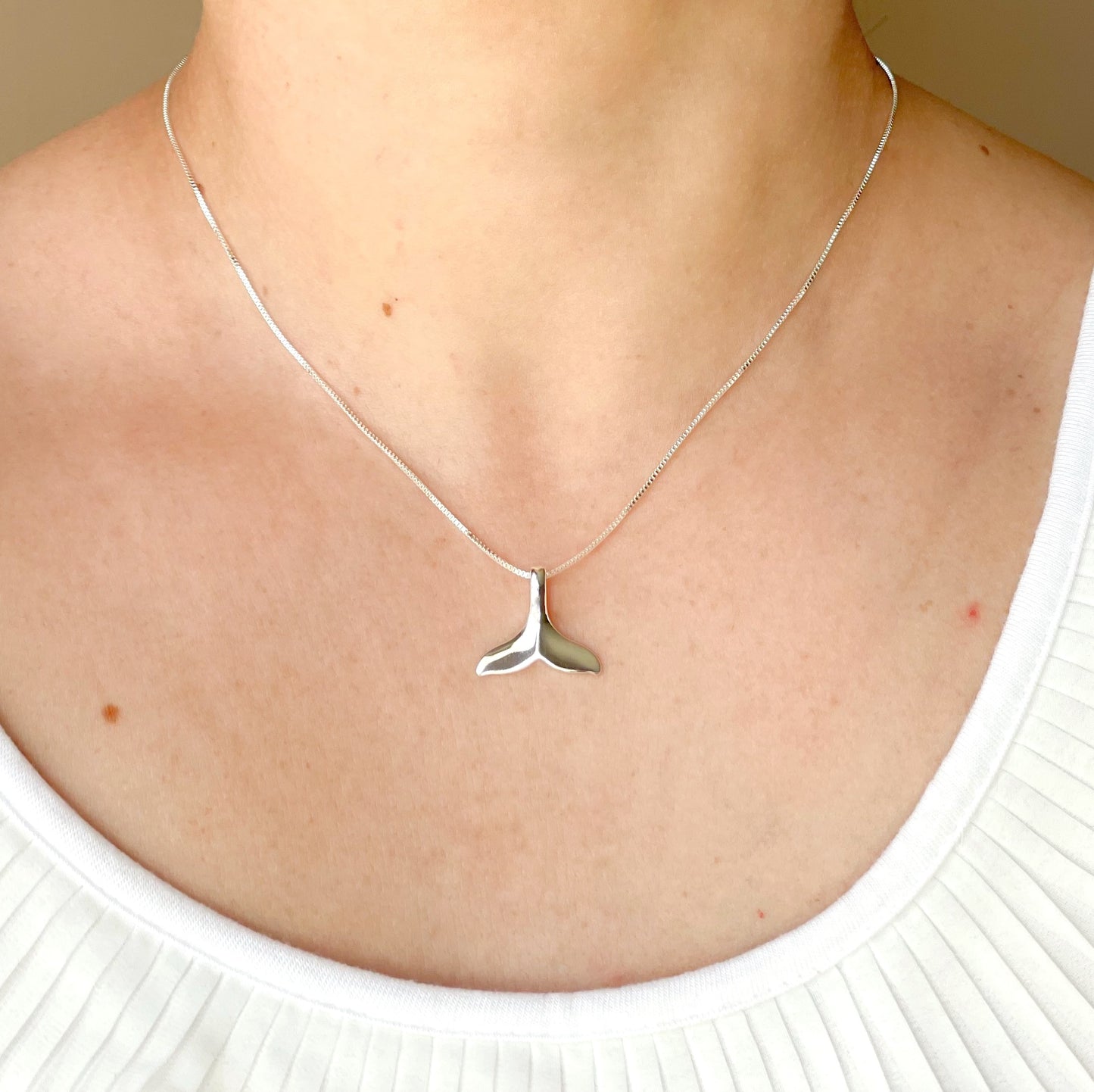 Silver whale tail necklace on a person wearing a white top.