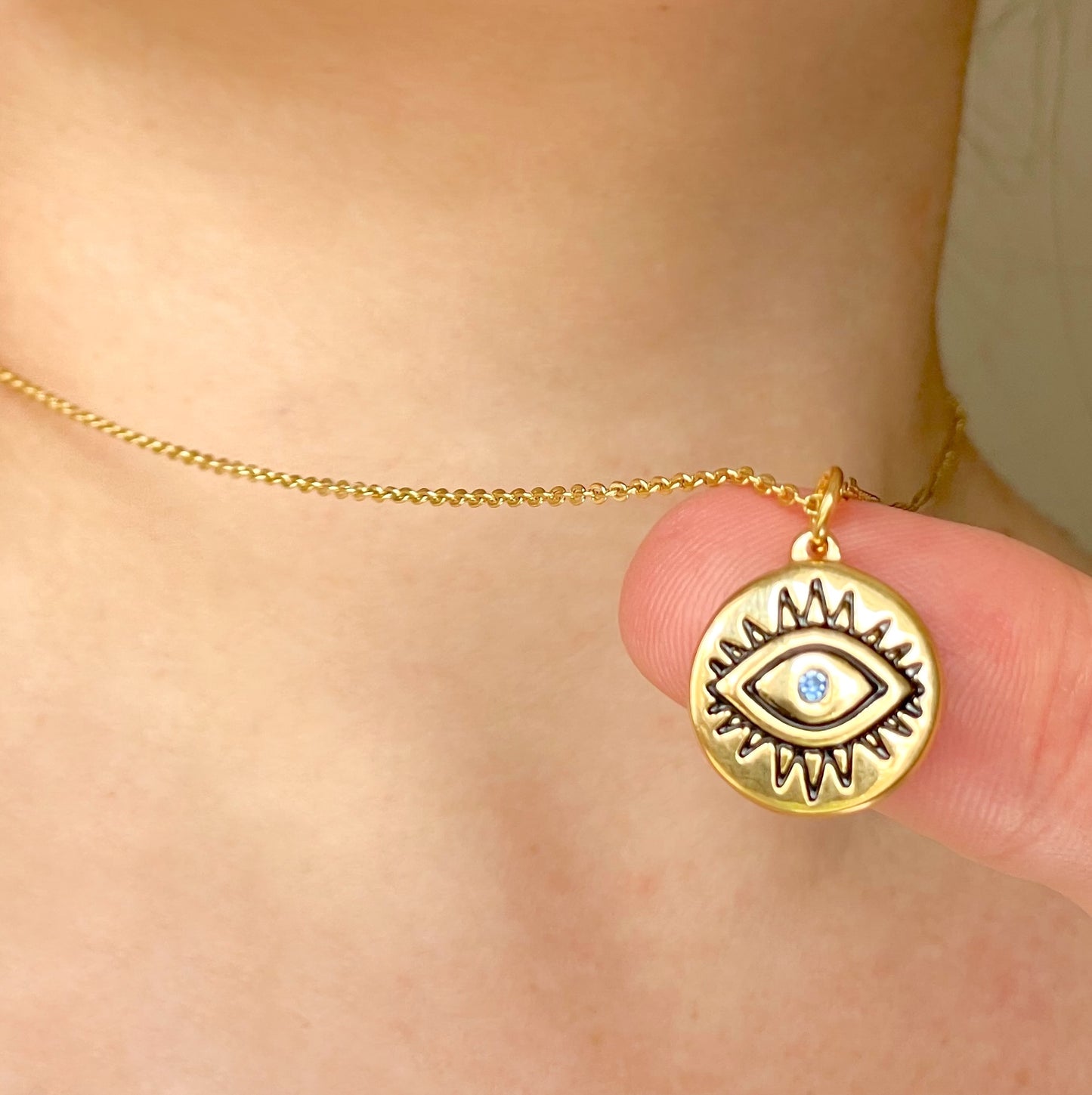 Gold necklace with an eye-shaped pendant and cable chain held by a hand against a neutral background