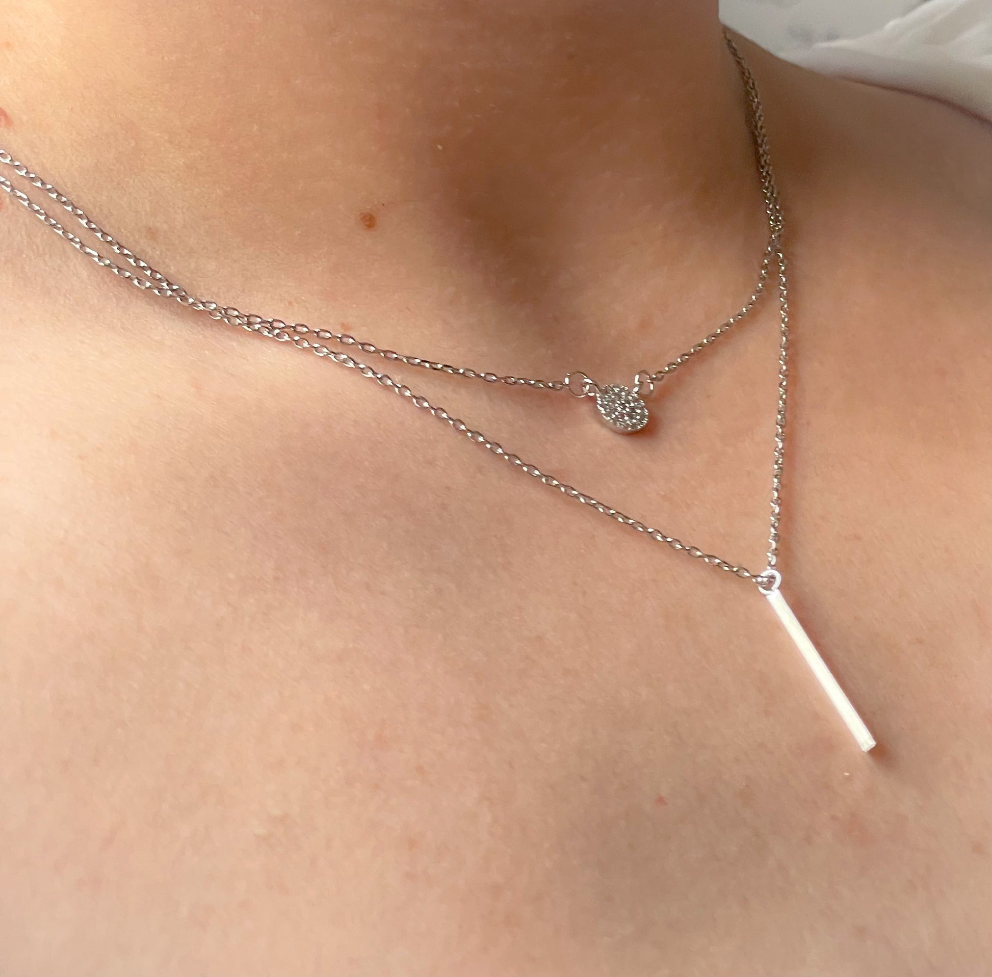 Side view of two in one necklace with different pendants on a person's neck with a close-up view of the skin.