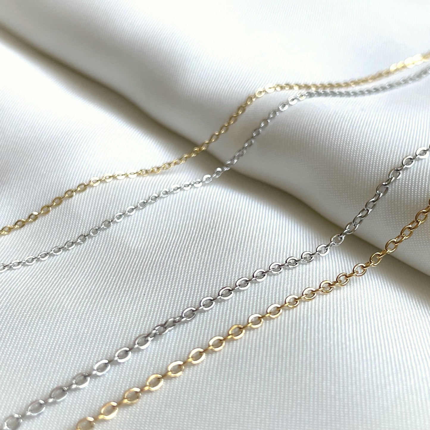 Two 1mm and two 1.5mm gold and silver cable chain necklaces on a white fabric background