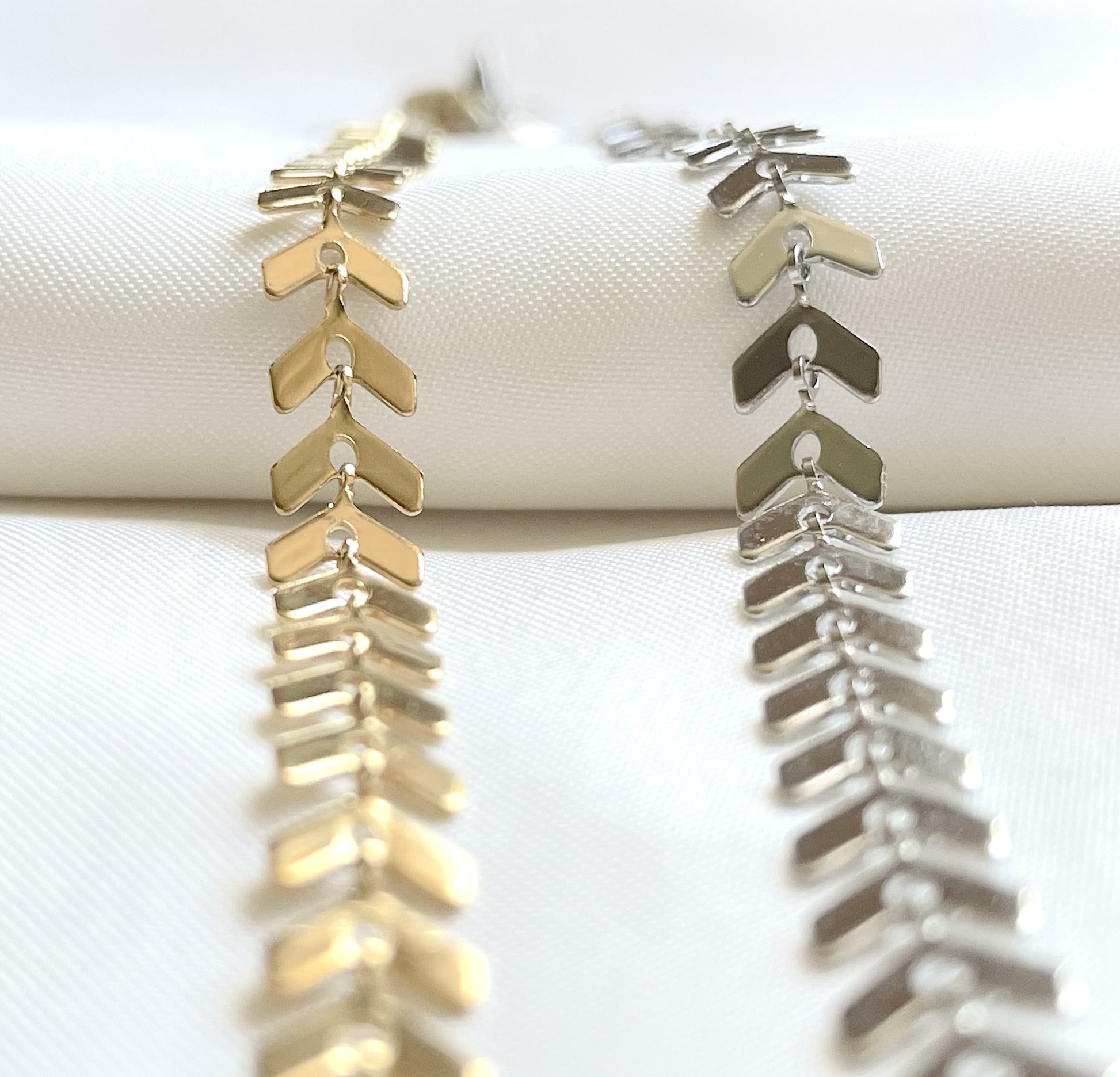 Gold and silver chevron anklets on a white surface