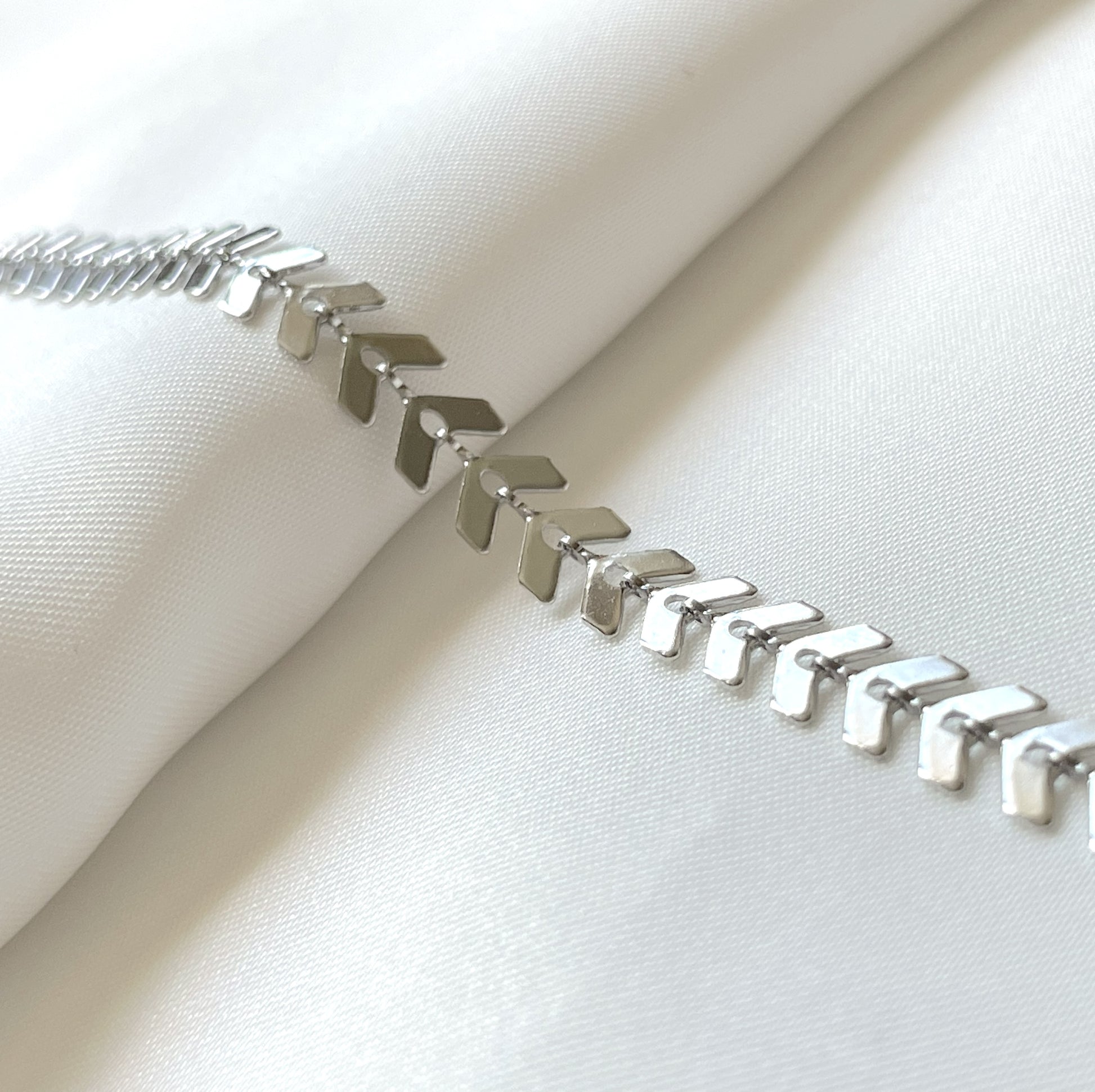 Silver leaf chain anklet on a white fabric background