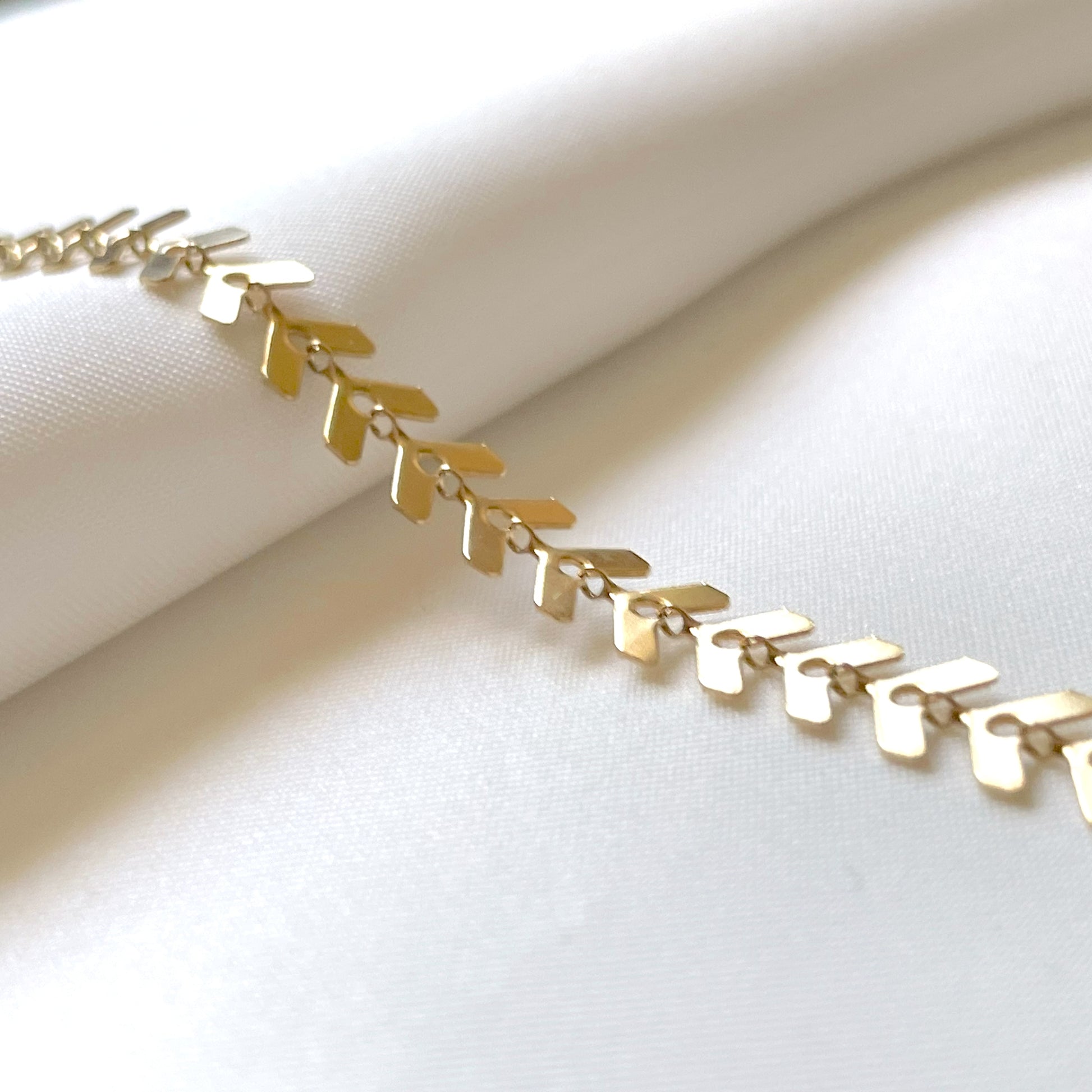 Gold fishbone chain anklet on a white fabric background
