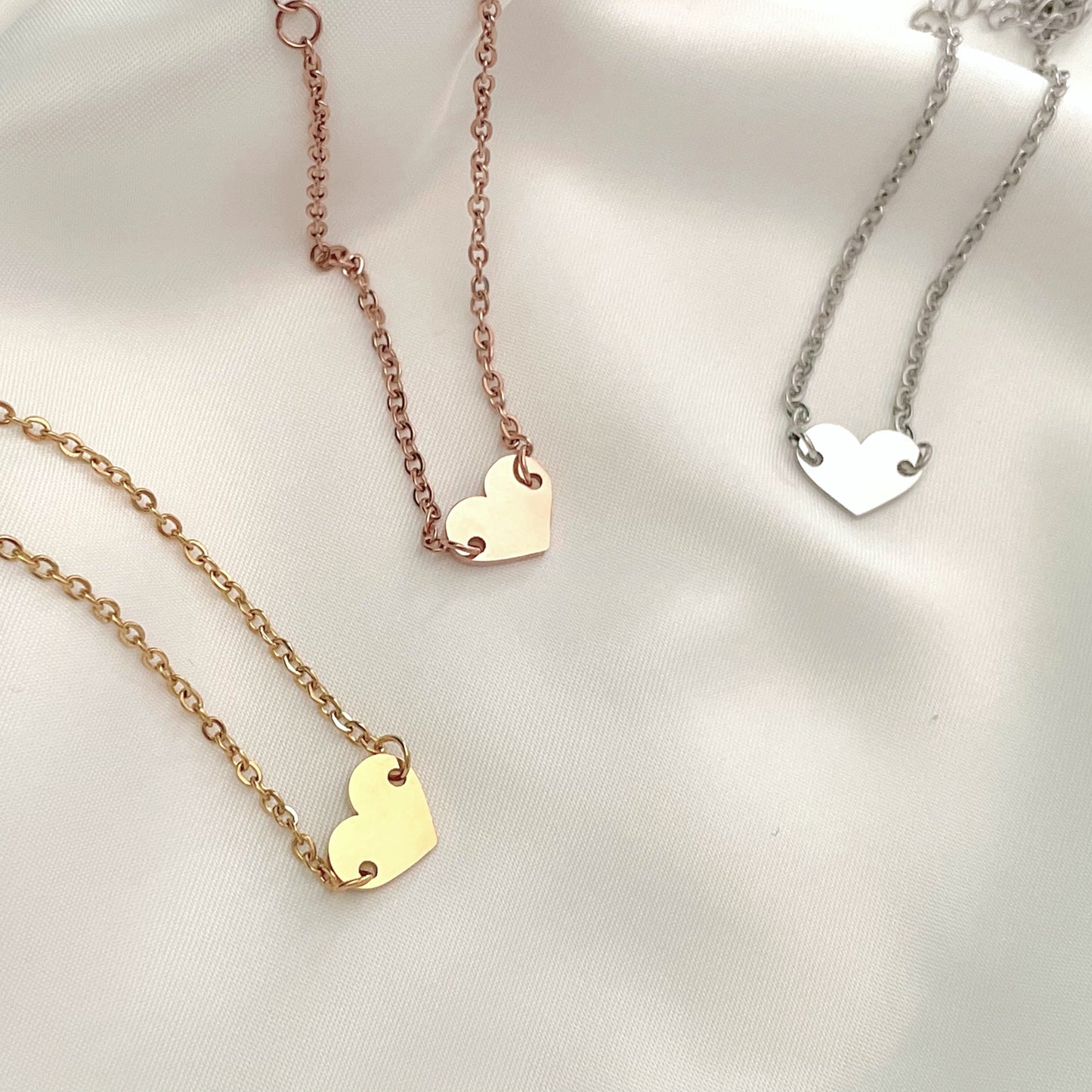 Three heart charm bracelets on gold, rose gold, and silver cable chains against a light background.