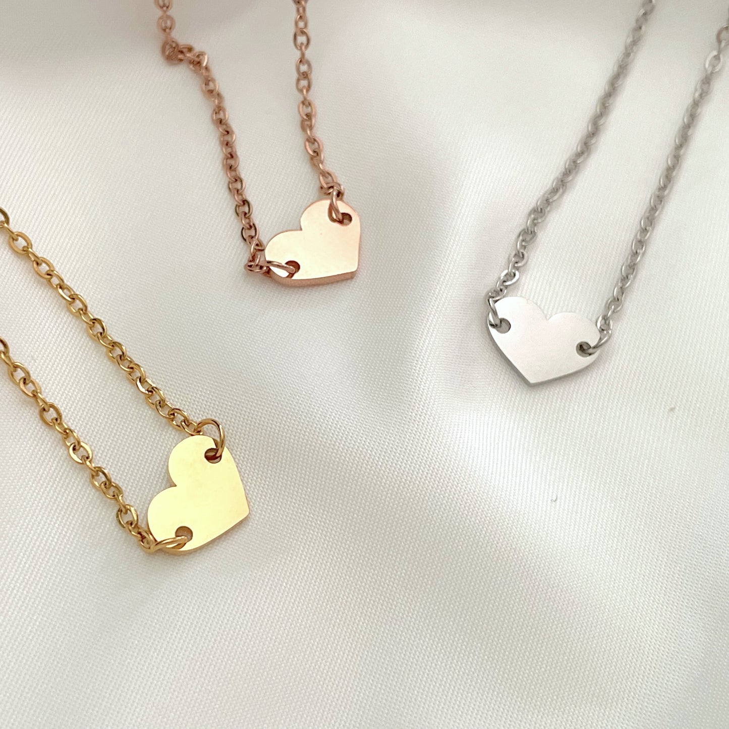 Three heart-shaped charm bracelets on gold, rose gold, and silver chains against a white background.