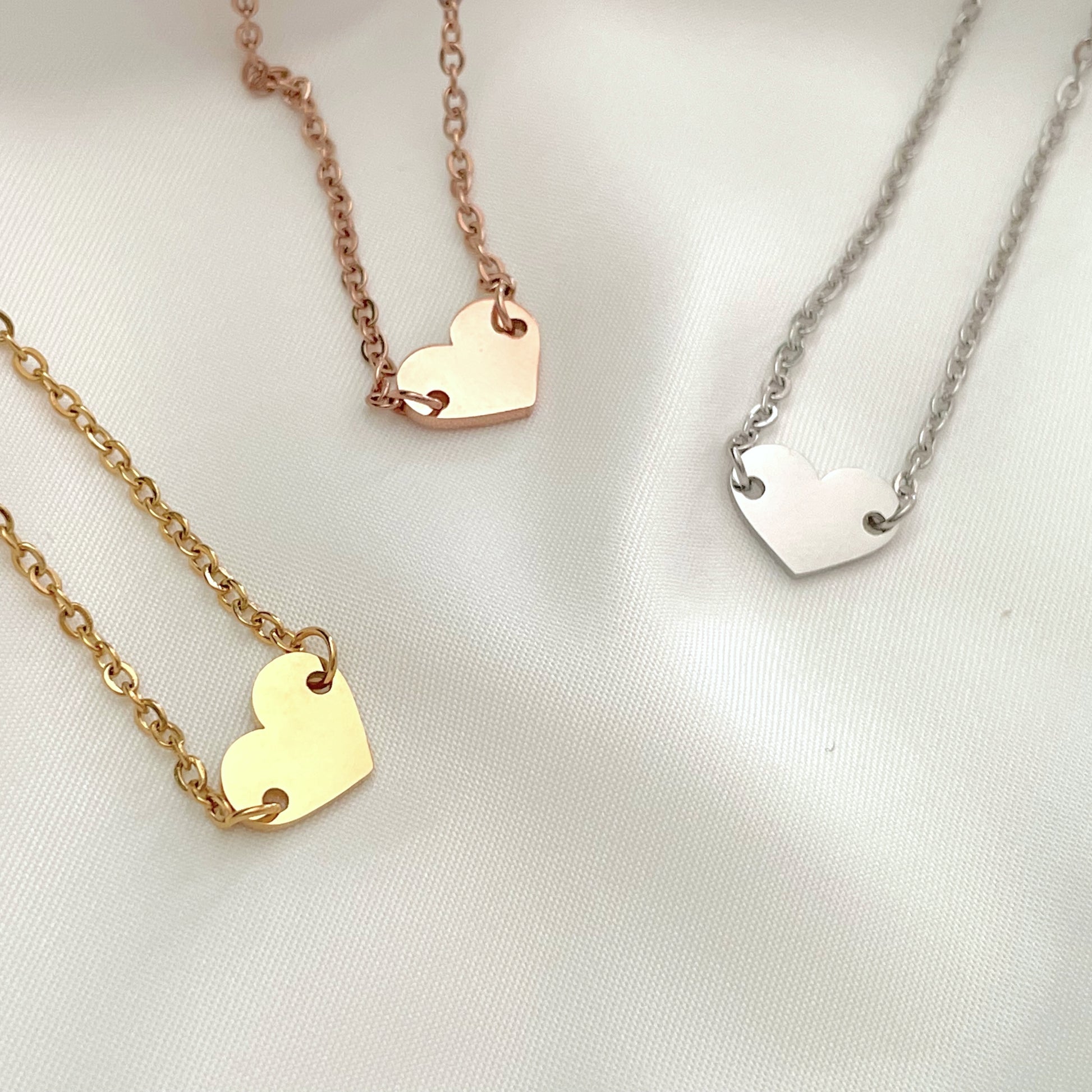 Three heart-shaped charm bracelets on gold, rose gold, and silver chains against a white background.