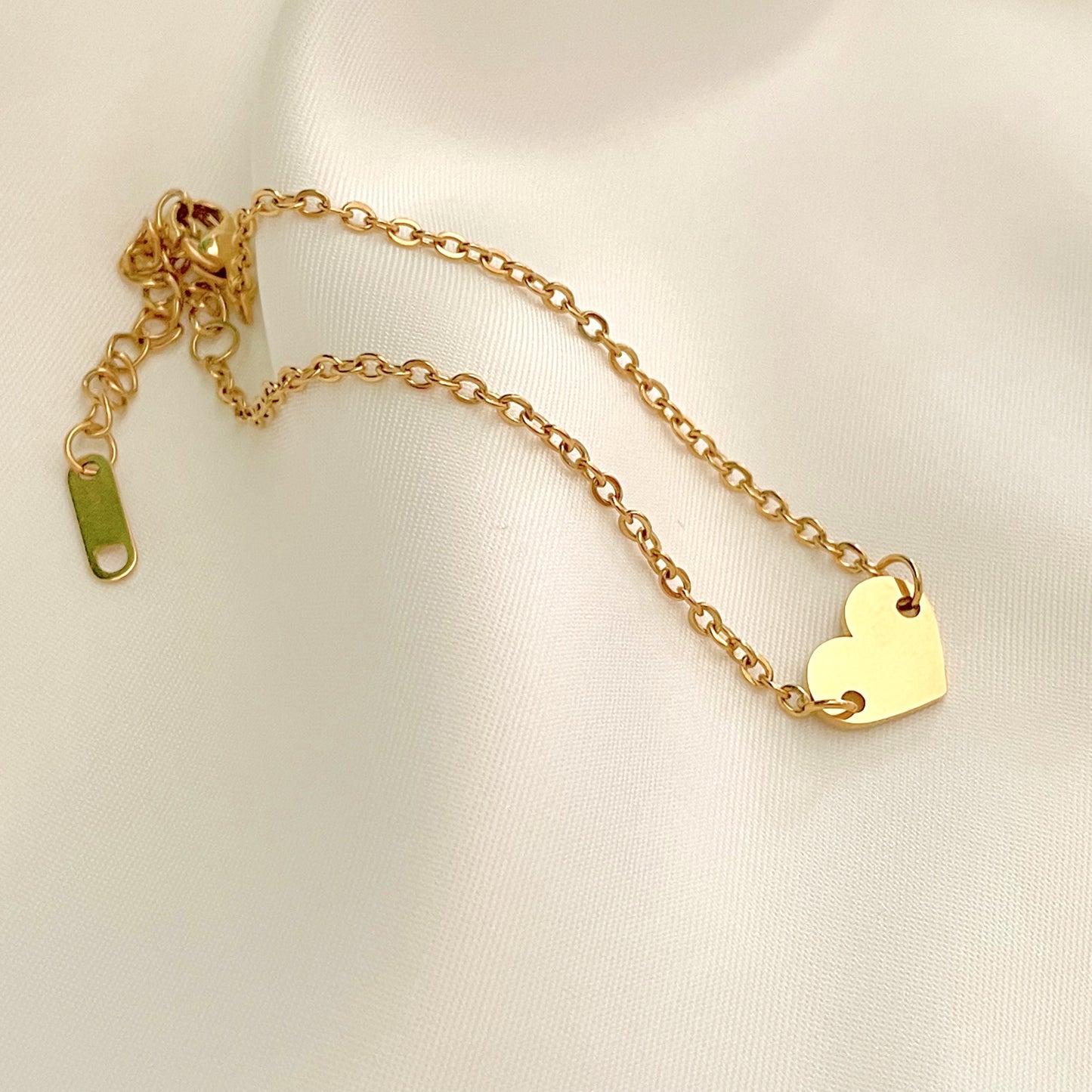 Gold bracelet with a medium flat hear charm on a light beige background