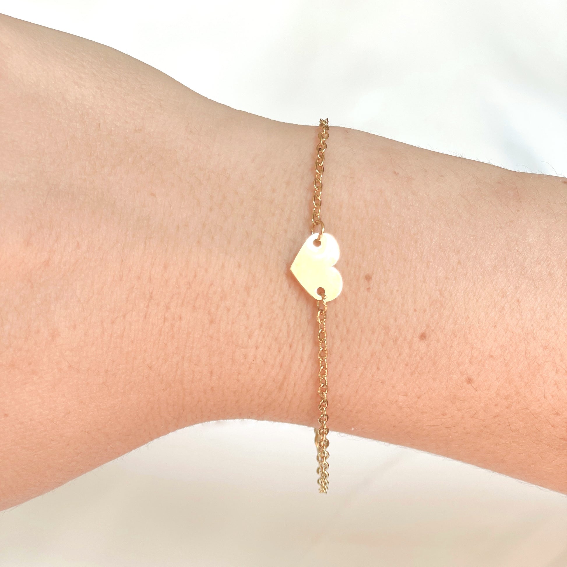Side view of gold heart bracelet on a wrist against a white background