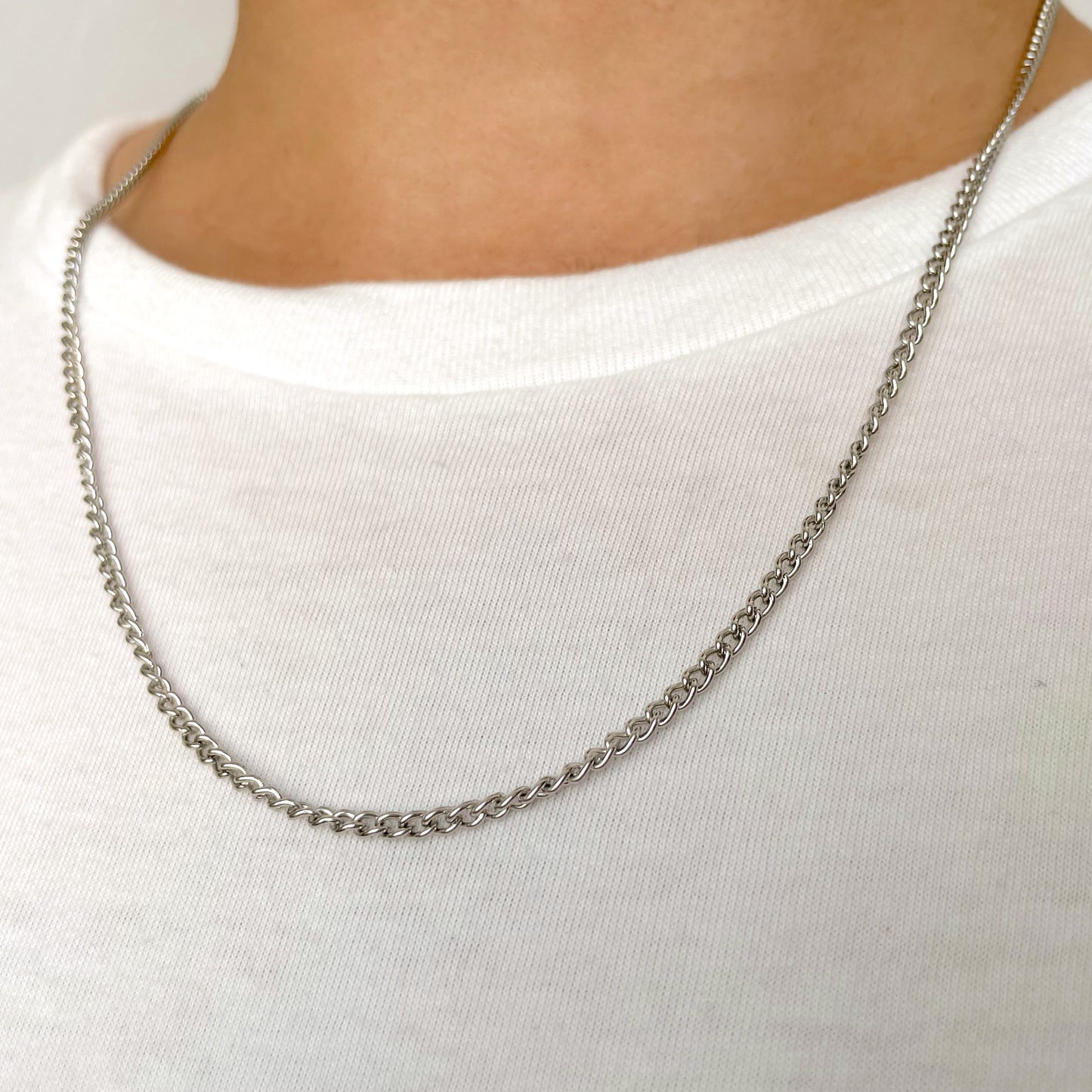 Long silver chain necklace worn by a man on a white background