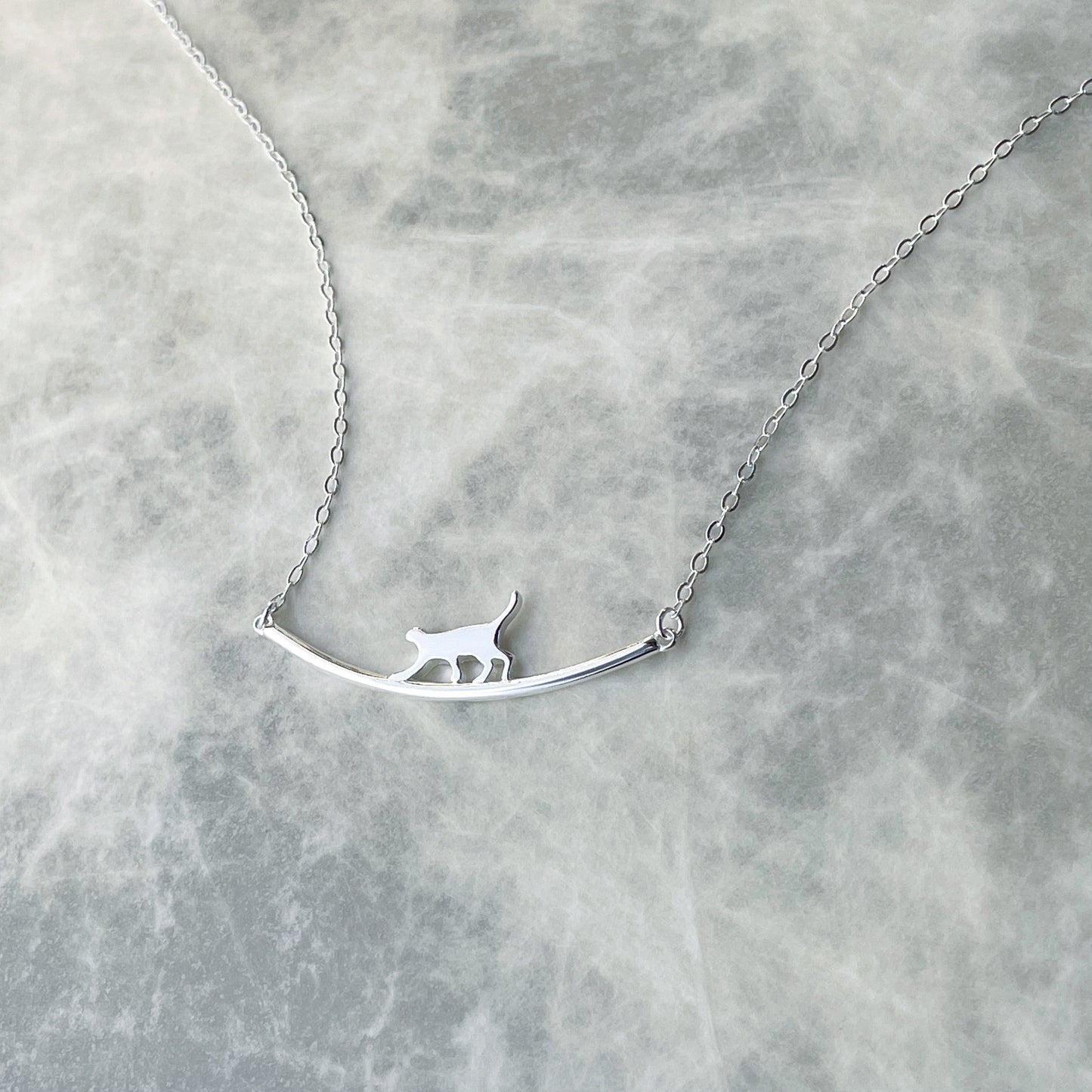 Silver necklace with a cat-shaped pendant on a marble surface