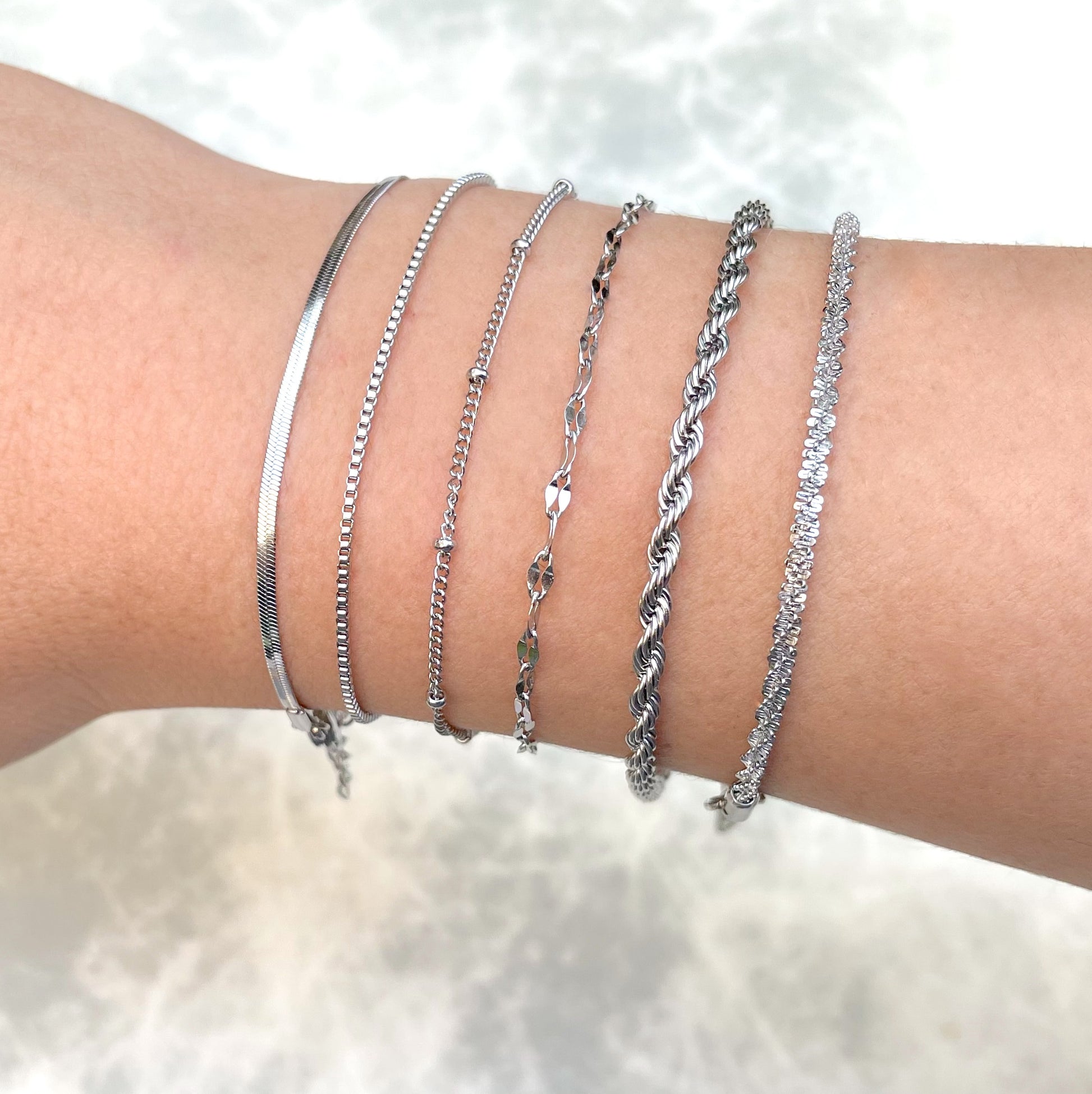 Collection of silver bracelets on a wrist against a soft white background