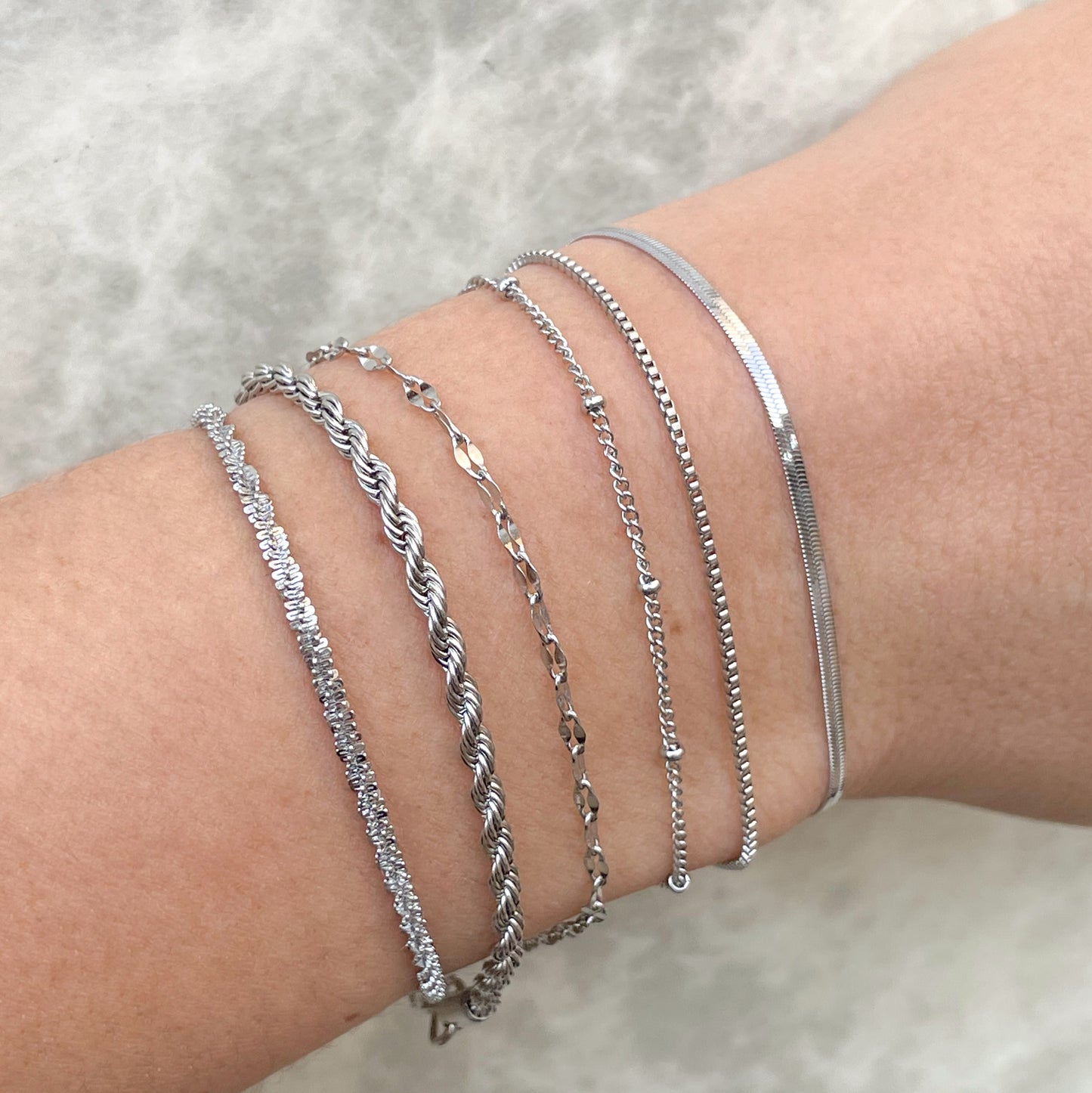 Silver bracelets on a wrist against a neutral background