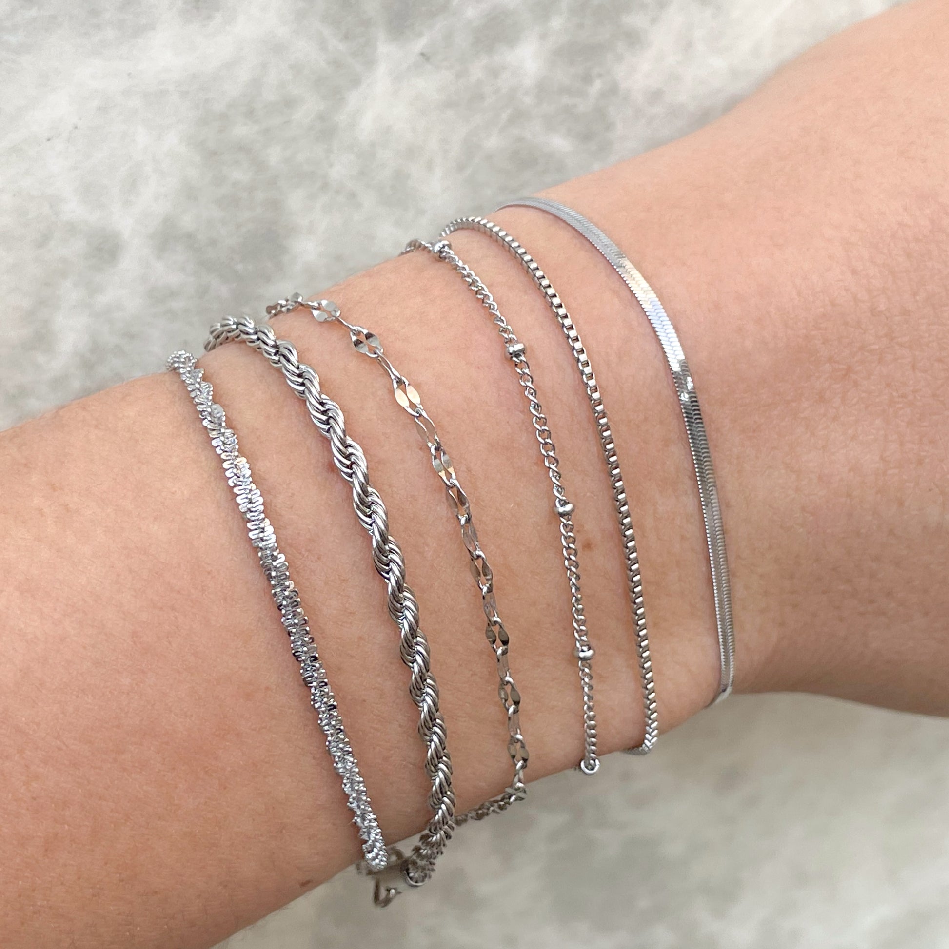 Silver bracelets on a wrist against a neutral background