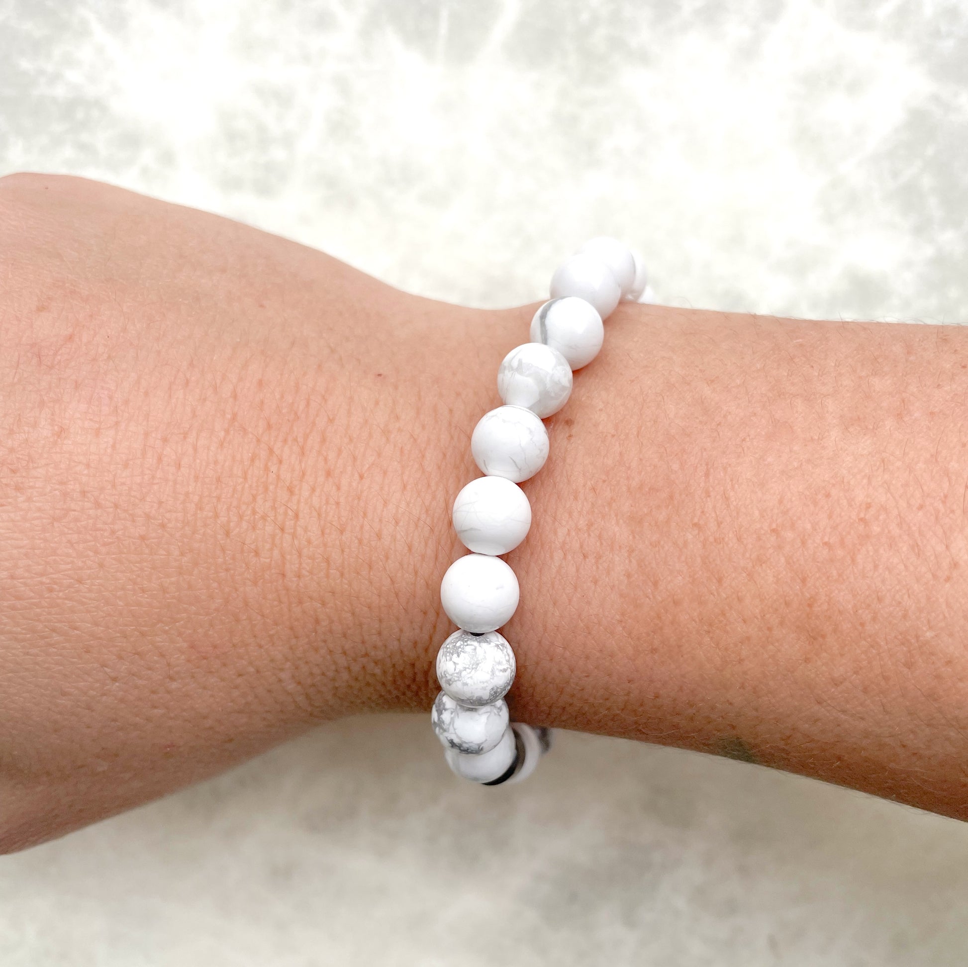 Side view of white beaded bracelet on a wrist against a white background