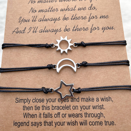 Three black cord bracelets with sun, star and moon charms on a brown card with text.