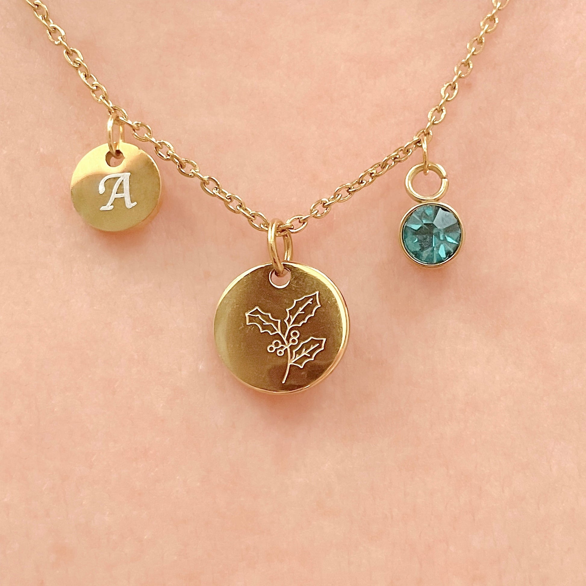 Gold necklace with three pendants, a small disc initial, december birth flower and birthstone on a women's neck