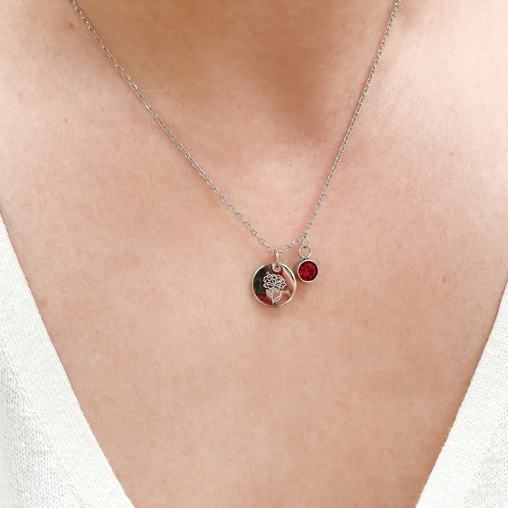 Silver Necklace with two charms, one coin with engraved birth flower and one bezel birthstone on a person's neck against a white background