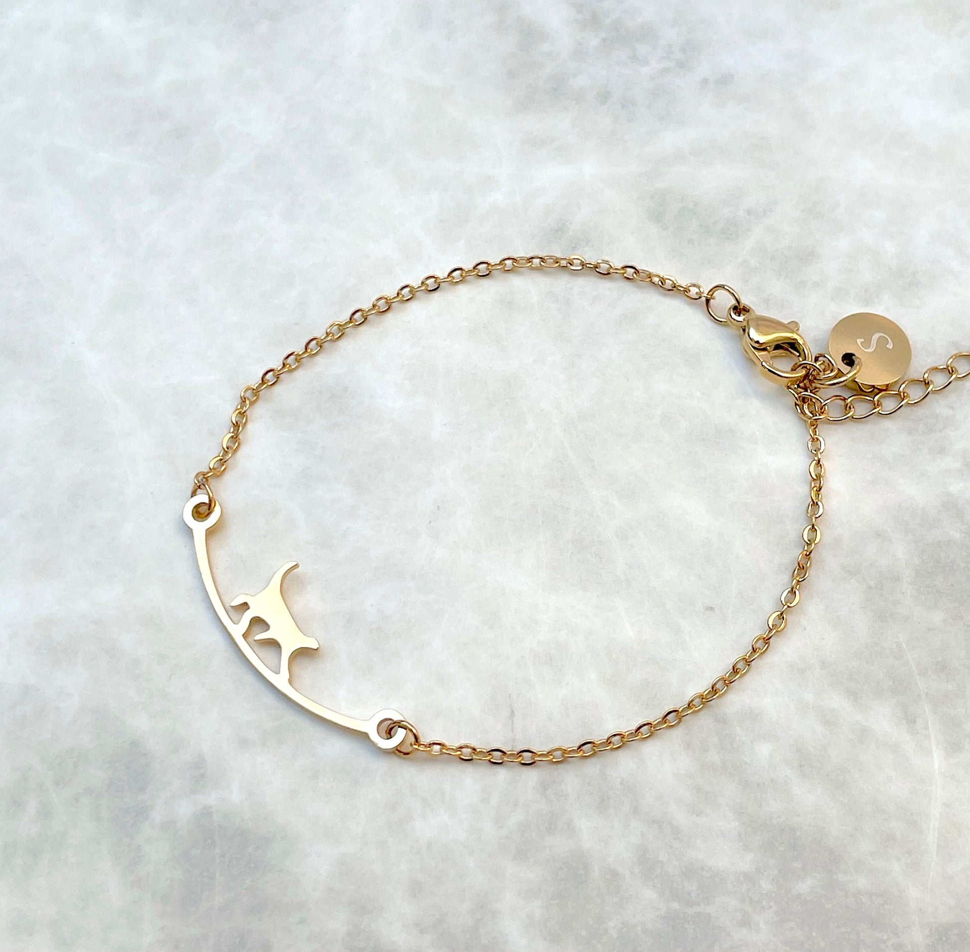 Top view of gold cat bracelet with an initial disc 'S' at the clasp on a light gray background