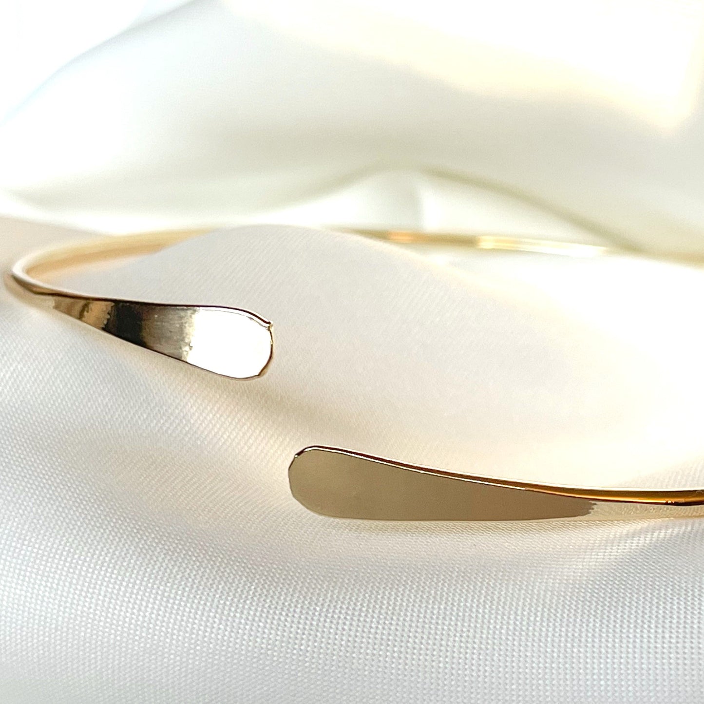 Gold arm cuff with flared ends on a white fabric background