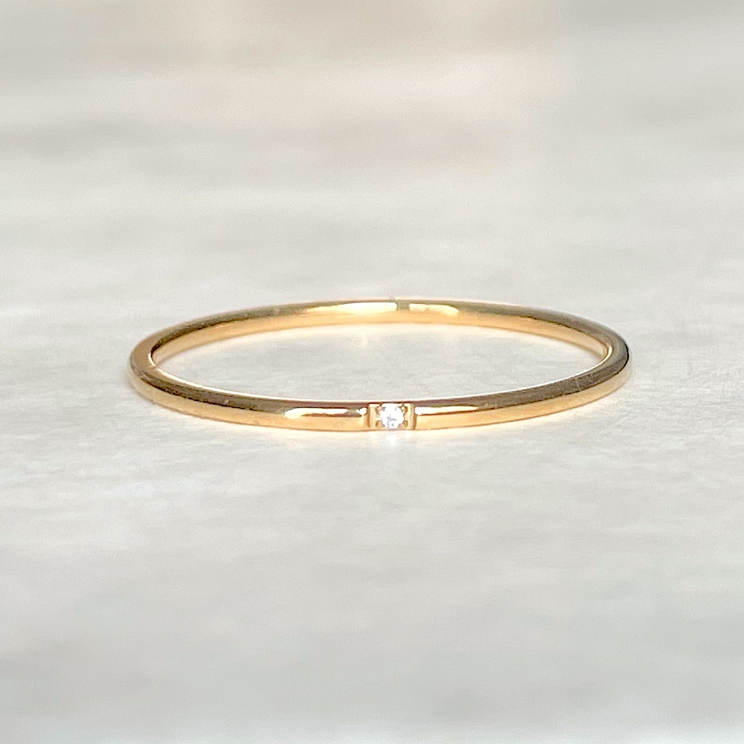 Front view of gold CZ ring with a small diamond on a light gray background