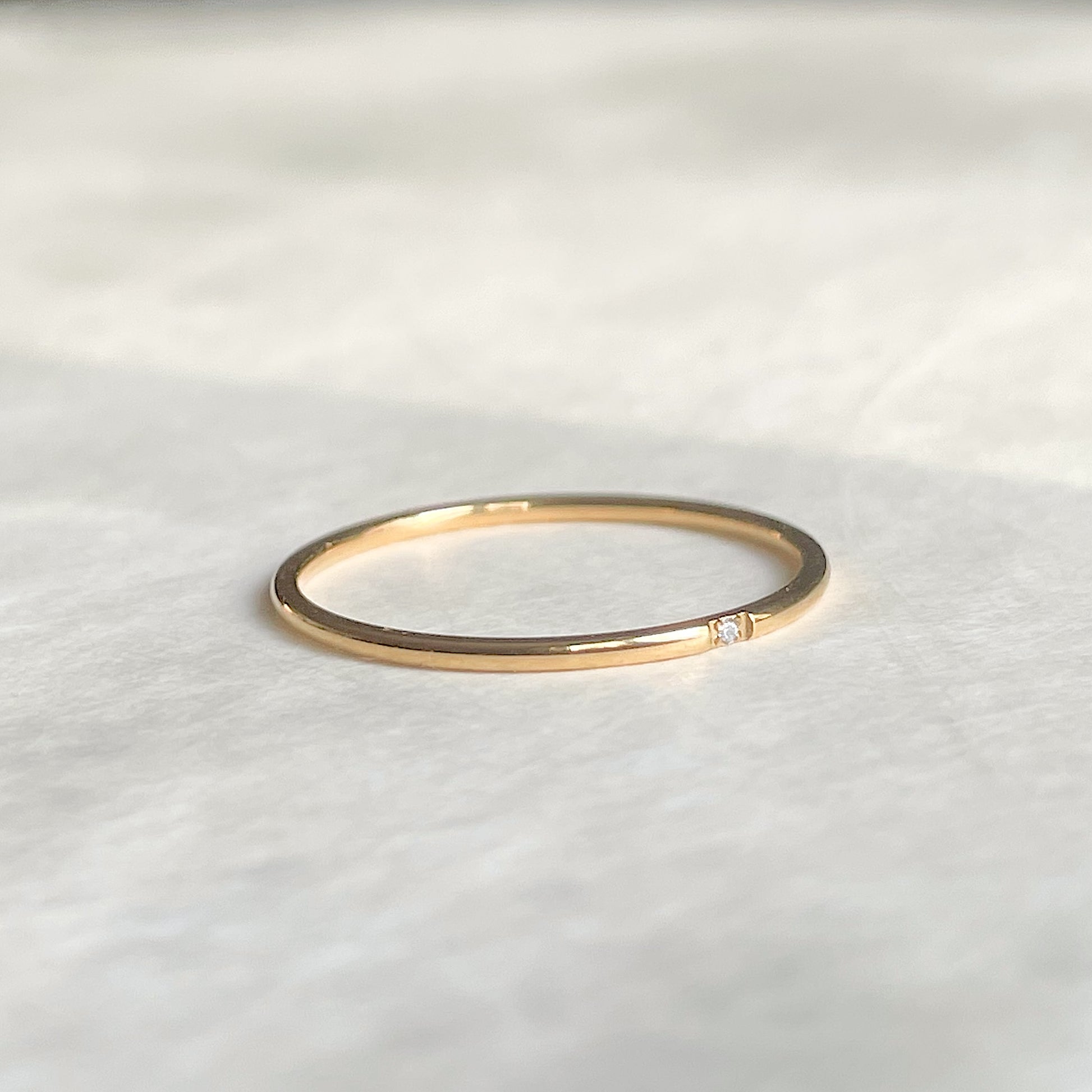 Angled front view of thin gold dimaond band on a white fabric background