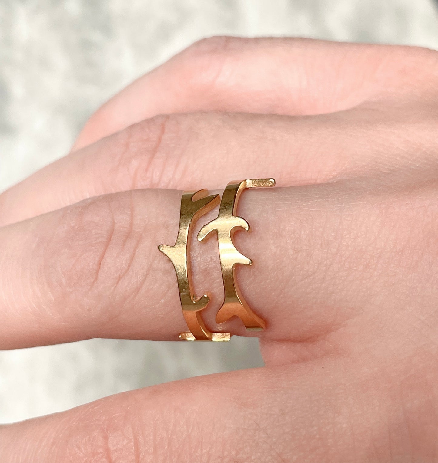 Side view of organic shape gold ring on a person's finger against a neutral background