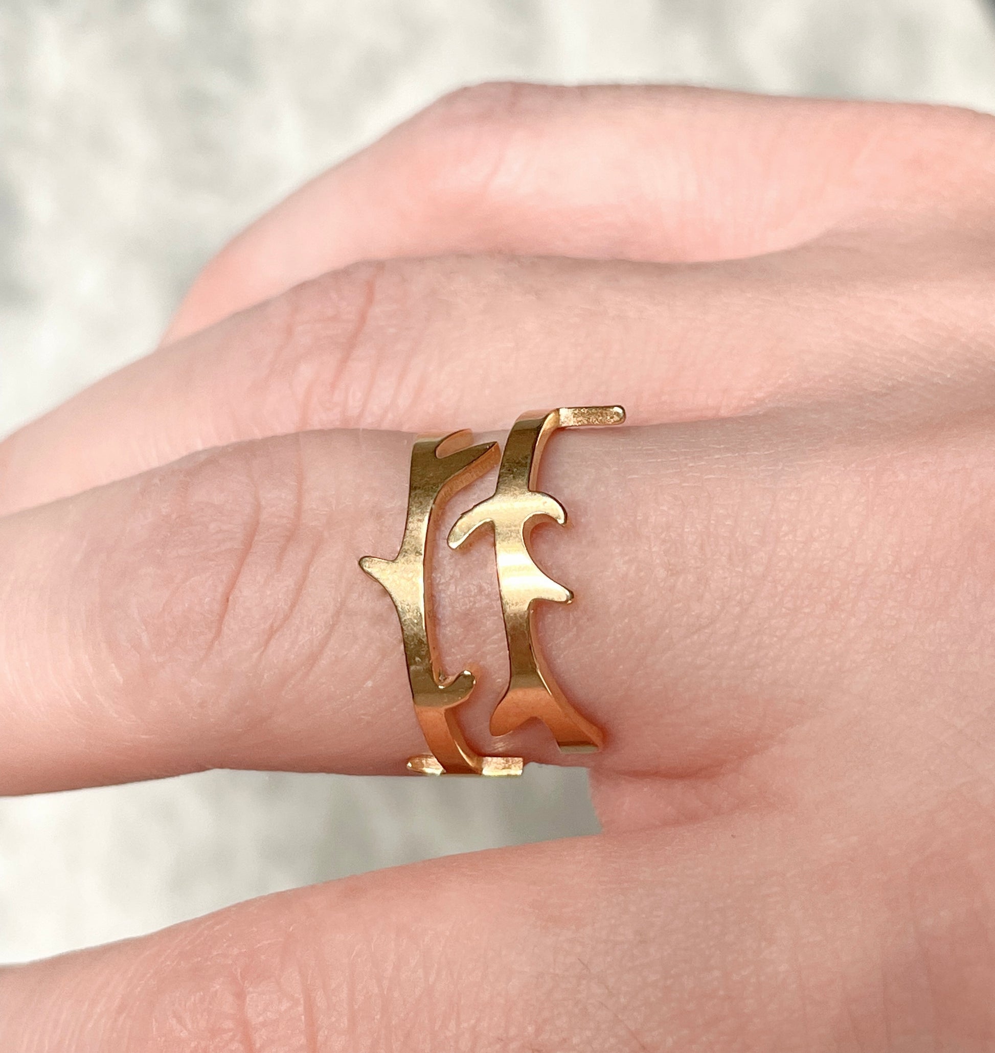Side view of organic shape gold ring on a person's finger against a neutral background
