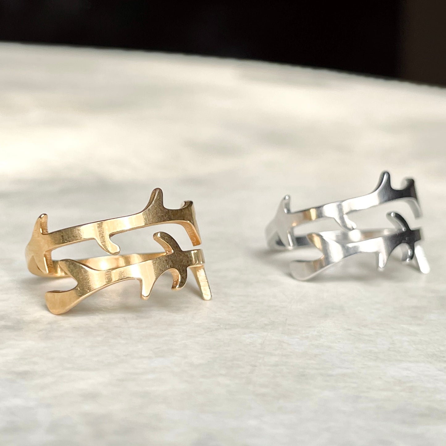 Front view of two gold and silver open rings on a textured surface