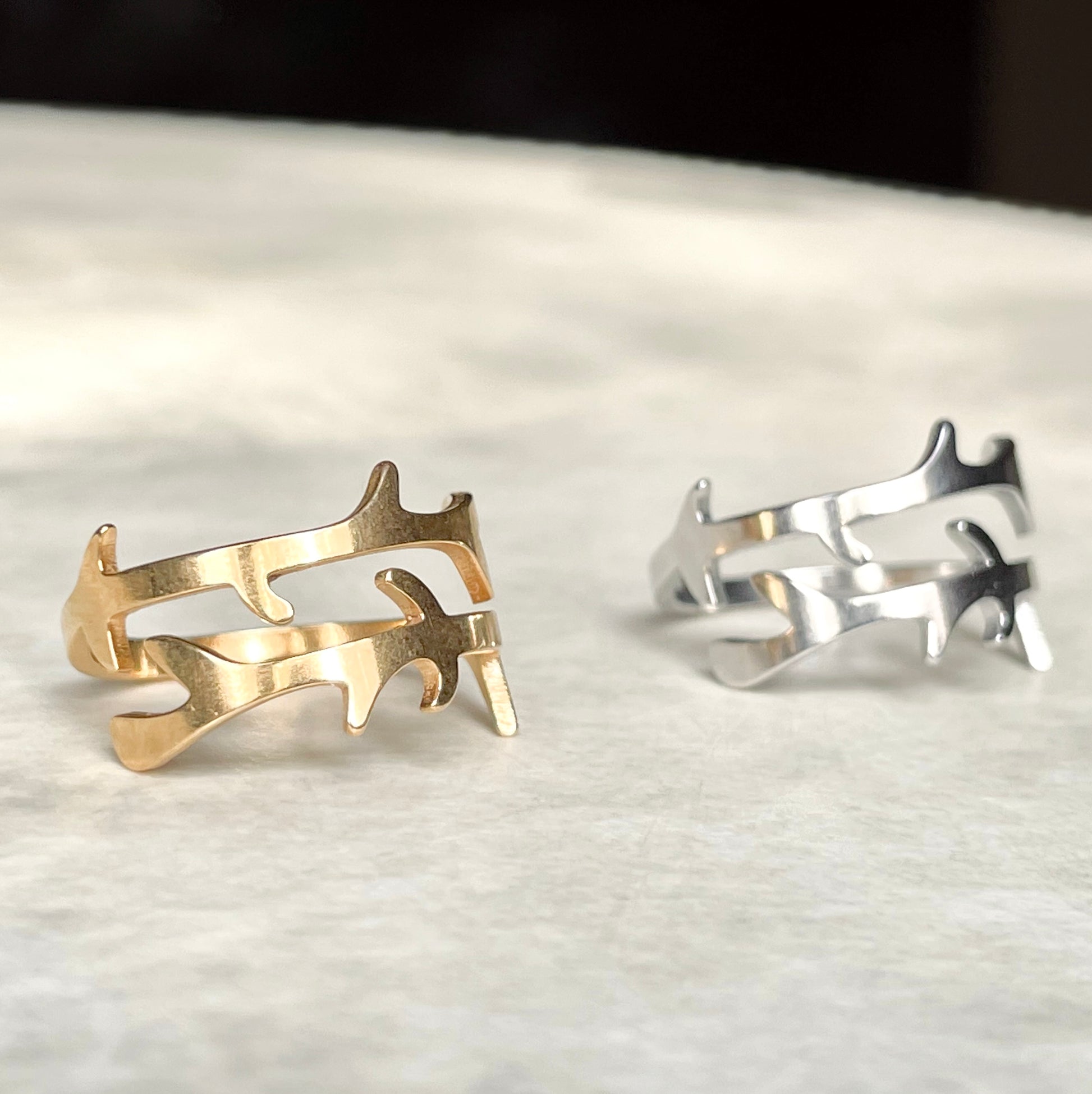Front view of two gold and silver open rings on a textured surface