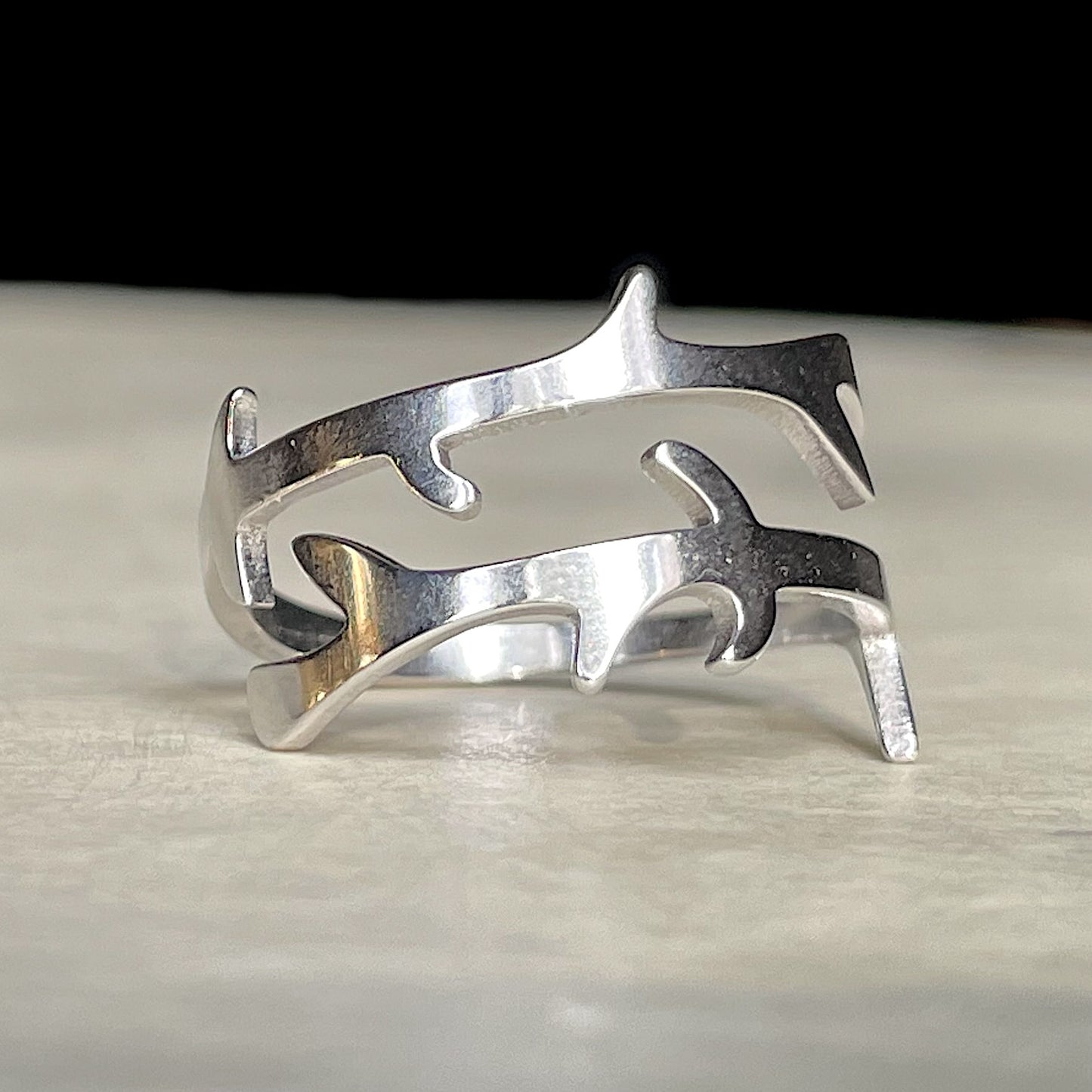 Nature-inspired silver crossover ring with a branch design on a light wooden surface