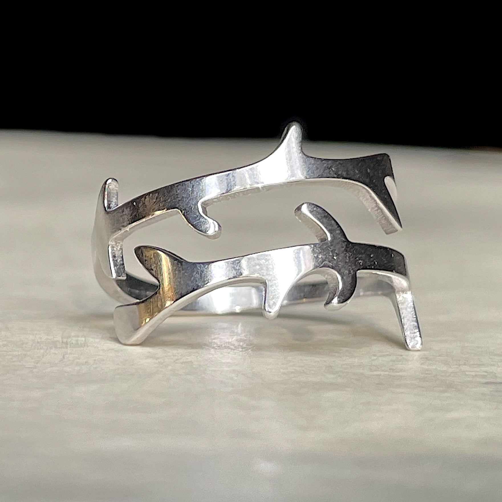 Nature-inspired silver crossover ring with a branch design on a light wooden surface