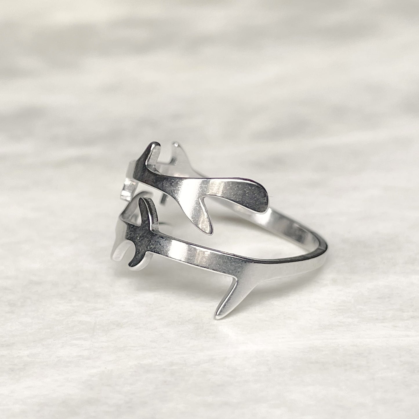 Side view of layered open crossover ring in silver on a light gray surface