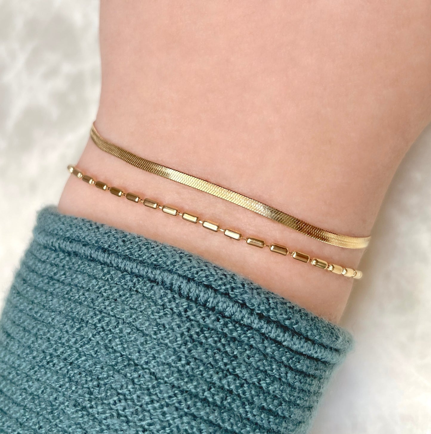 Close-up top view of two gold bracelets linked together on a wrist with a blue knitted sleeve