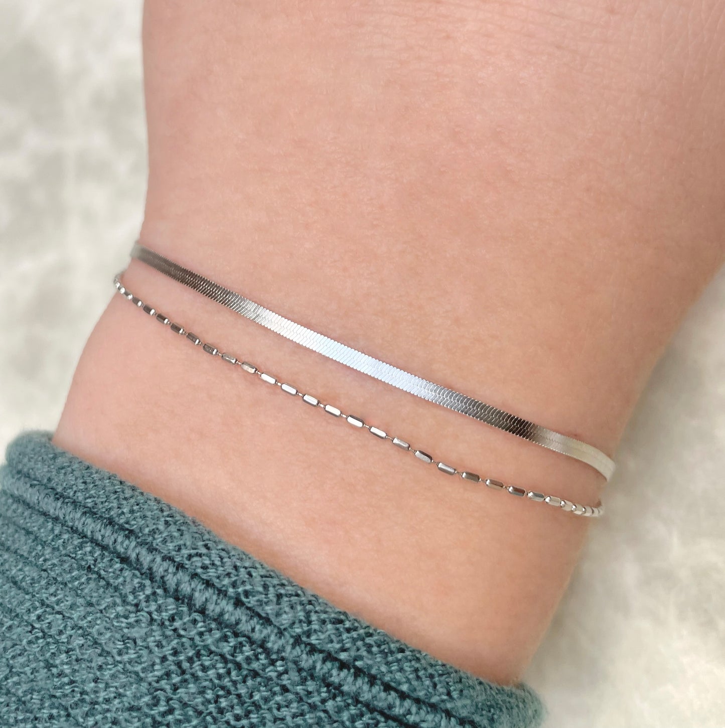 Double layered silver herringbone bracelet on a person's ankle with a soft background