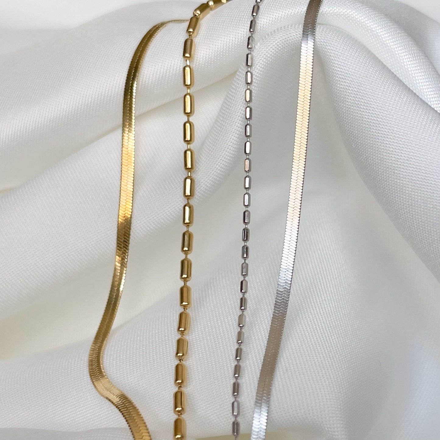 Two layered bracelets, one gold and one silver on a white fabric background