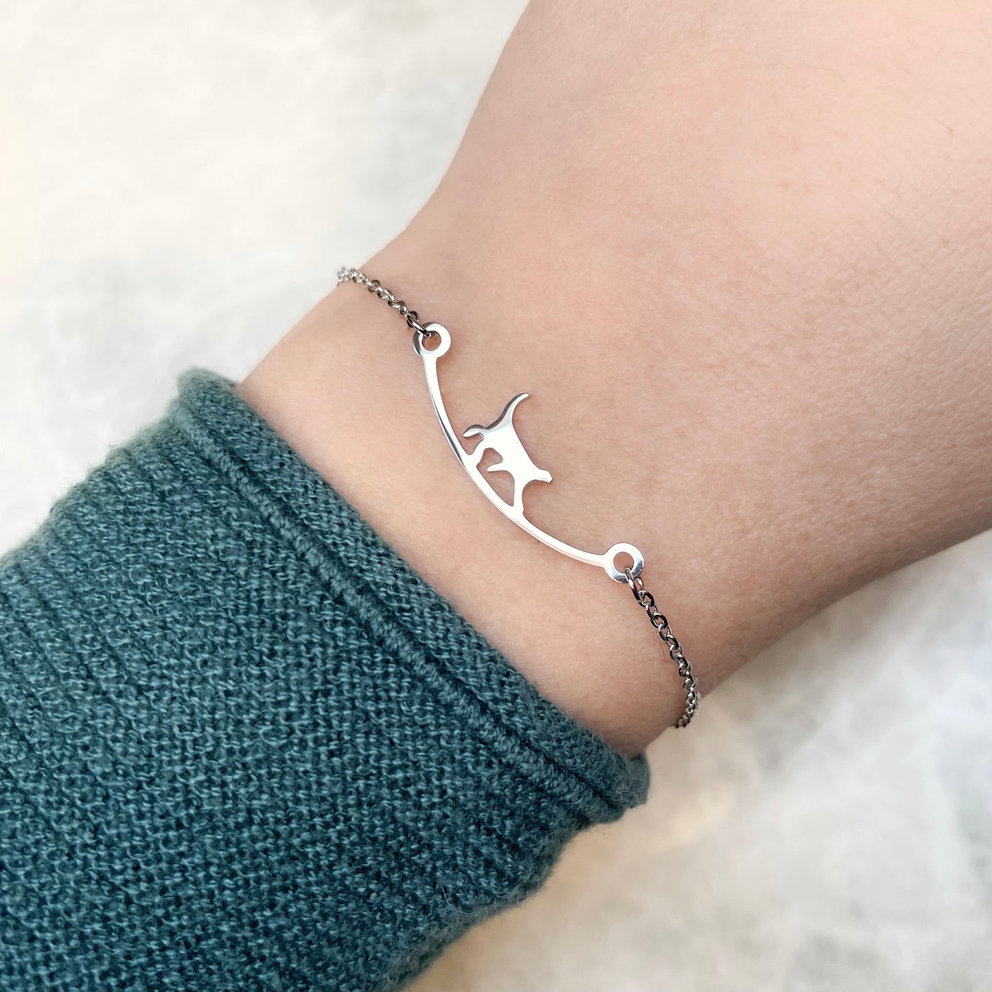 Silver bracelet with a cat design on a wrist against a white background