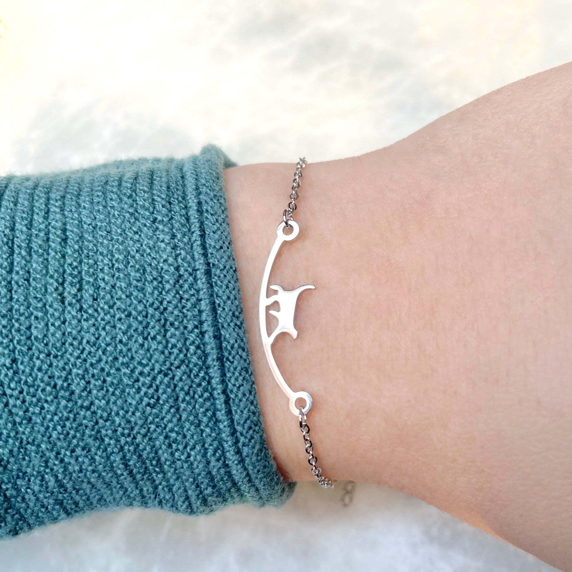 Side view of silver cat bracelet on a wrist with a blue sleeve