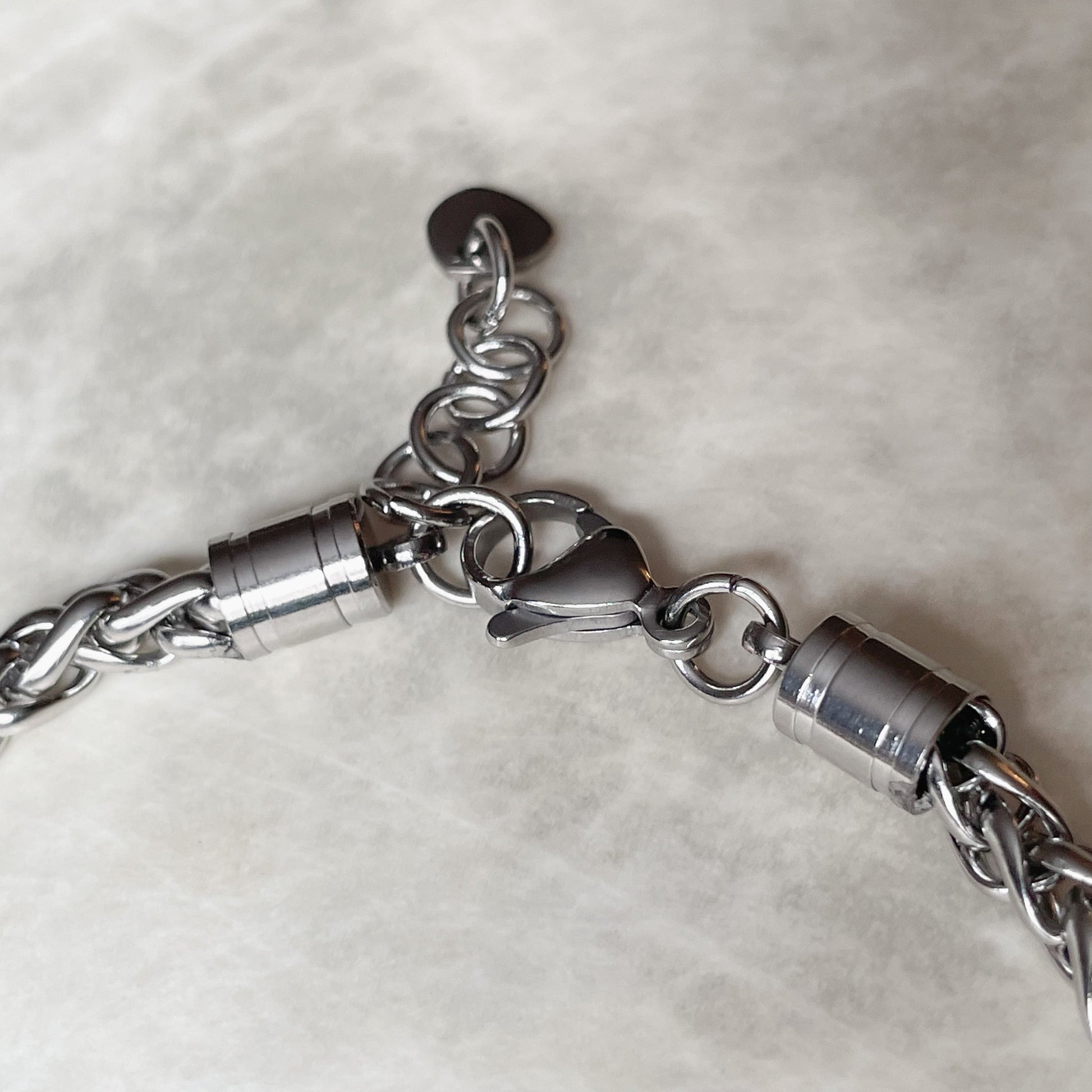 Close-up of the lobster claw clasp and one inch extender chain of the silver bracelet on a light gray background