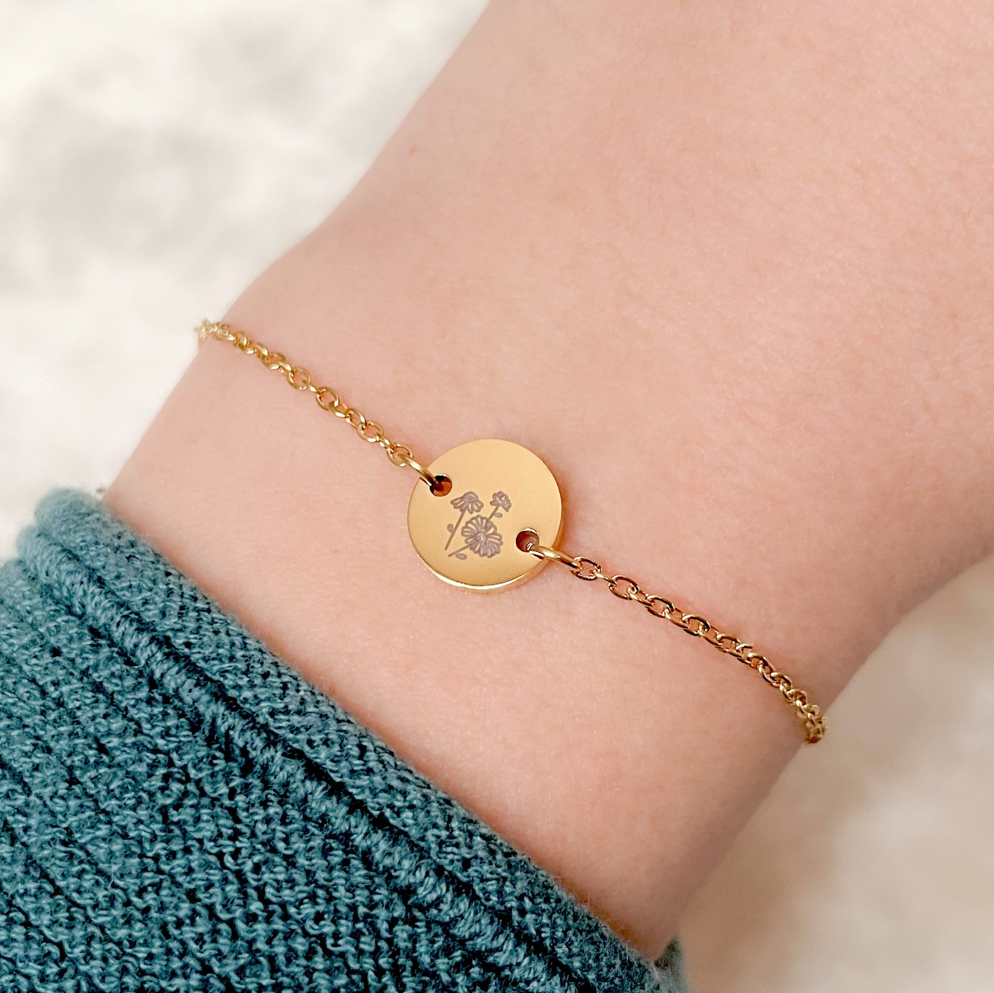 Gold april birth flower 'daisy' bracelet with a circular charm on a wrist against a neutral background