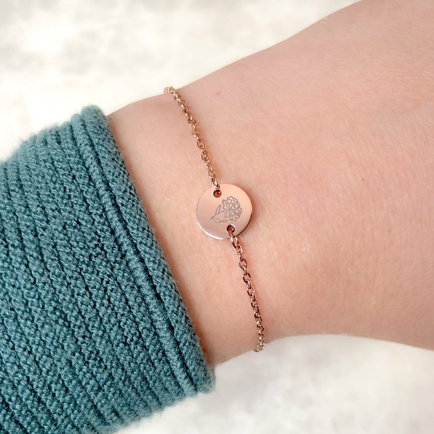 Rose gold January birth flower bracelet with a carnation engraving on wrist against a white background