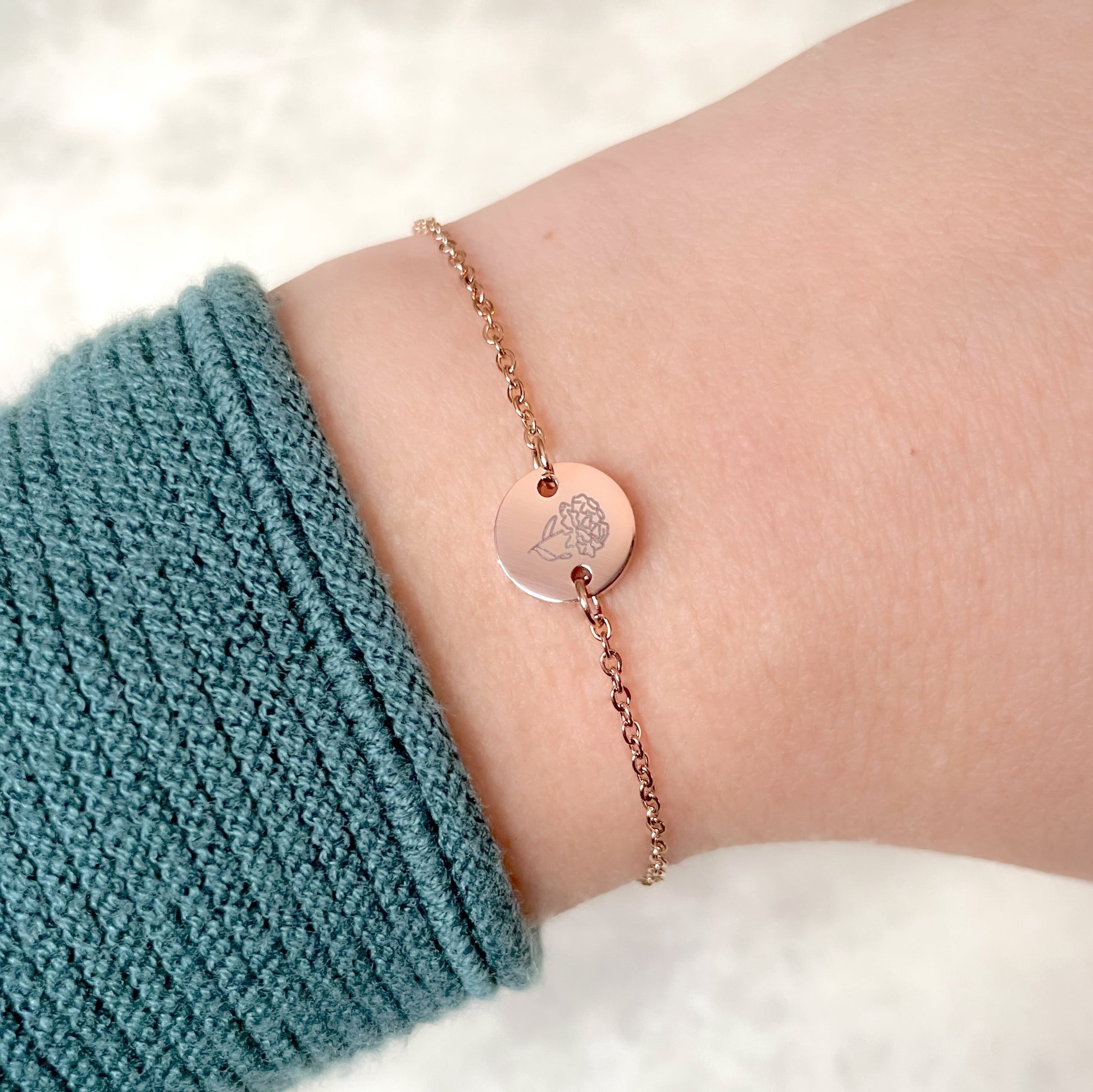 Rose gold January birth flower bracelet with a carnation engraving on wrist against a white background